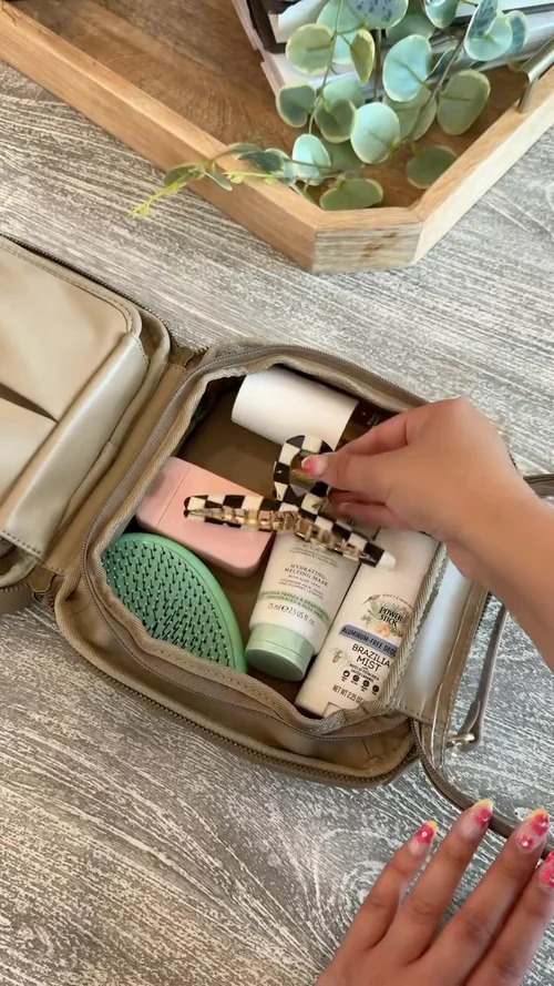 Open travel bag with toiletries and a hand placing a hair clip inside.