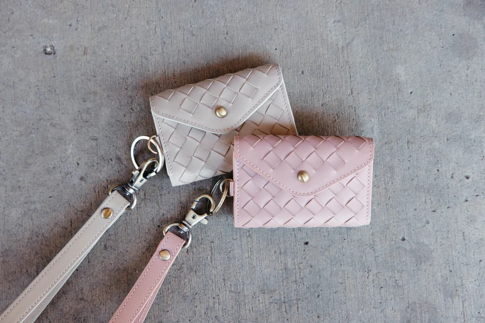Two woven leather cardholders with straps on a concrete surface.