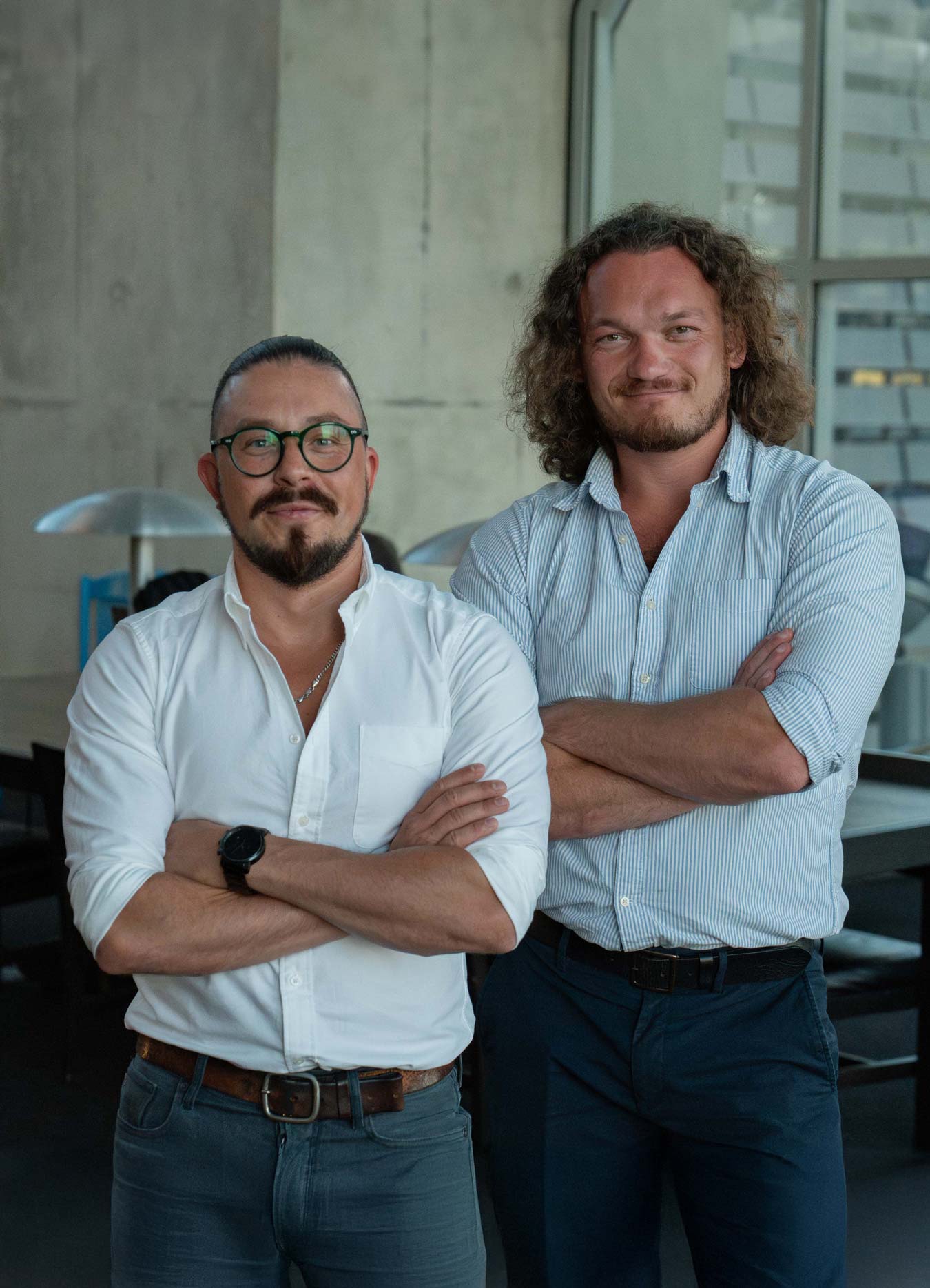 Two men standing with arms crossed, smiling in a modern office environment.