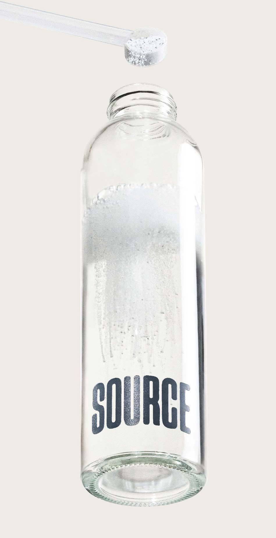 Transparent bottle labeled 'SOURCE' being filled with white powder from a scoop.