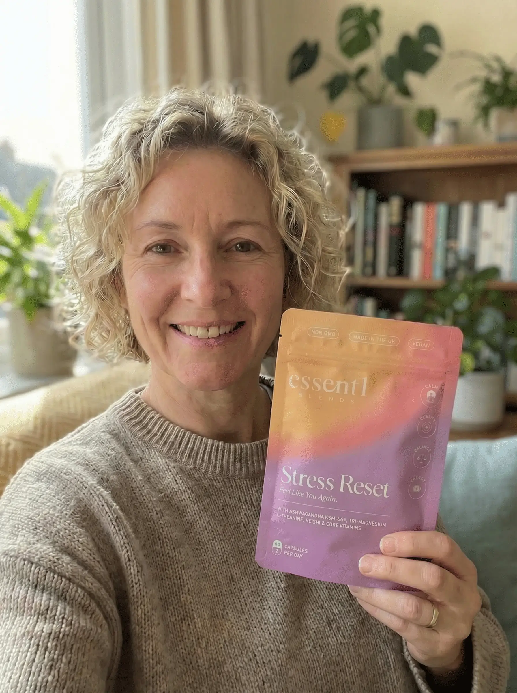 A smiling woman with blonde curly hair holds up a purple and orange pouch of Stress Reset supplements.
