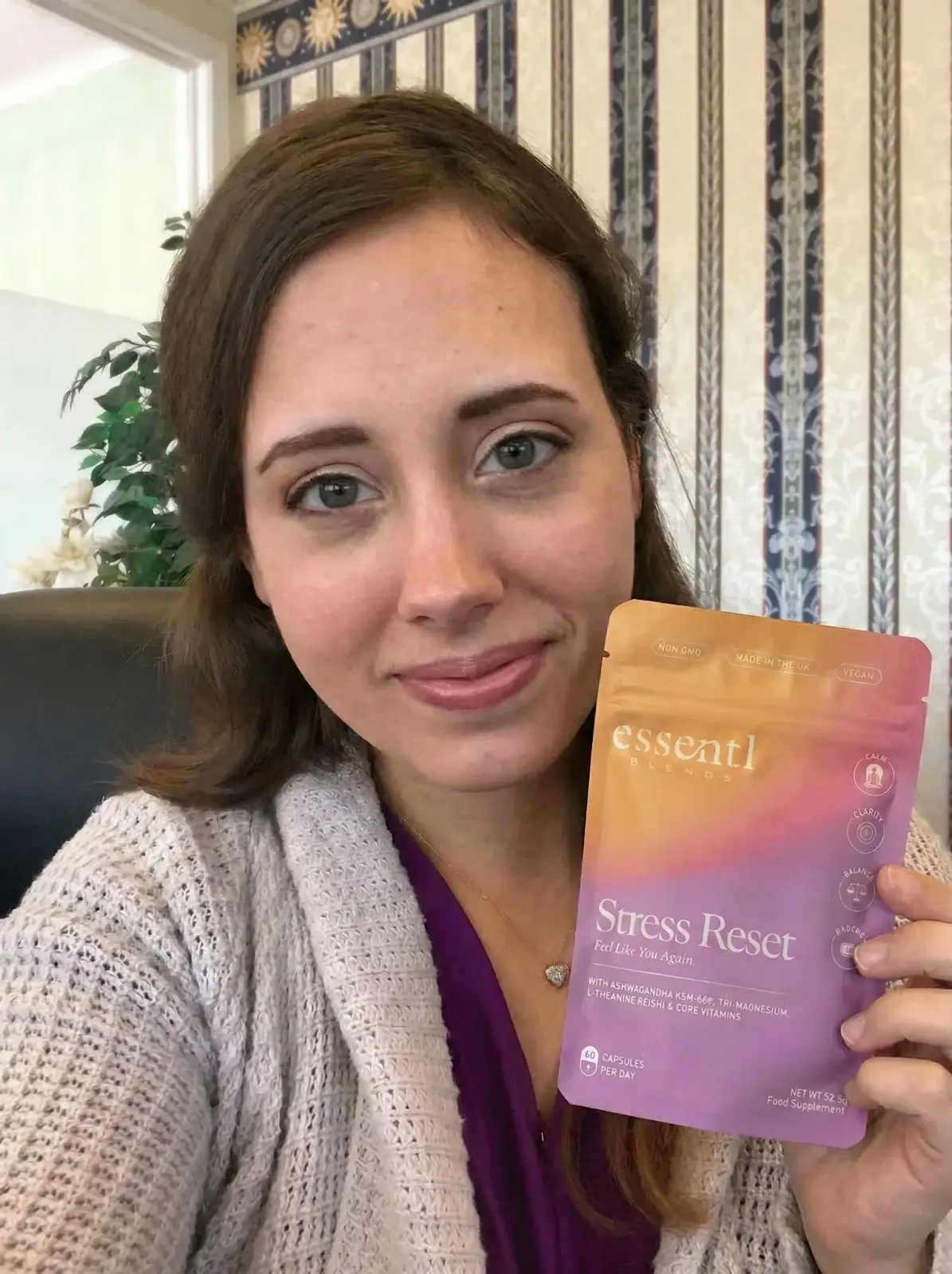 A woman with brown hair holds up a purple and orange pouch of Stress Reset food supplement.