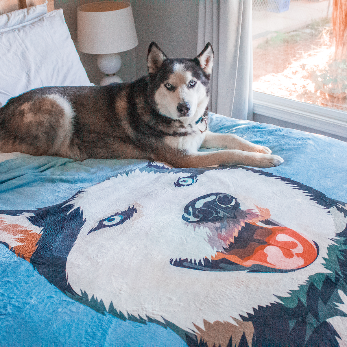 A dog rests on a bed covered with a personalized blanket displaying its face.