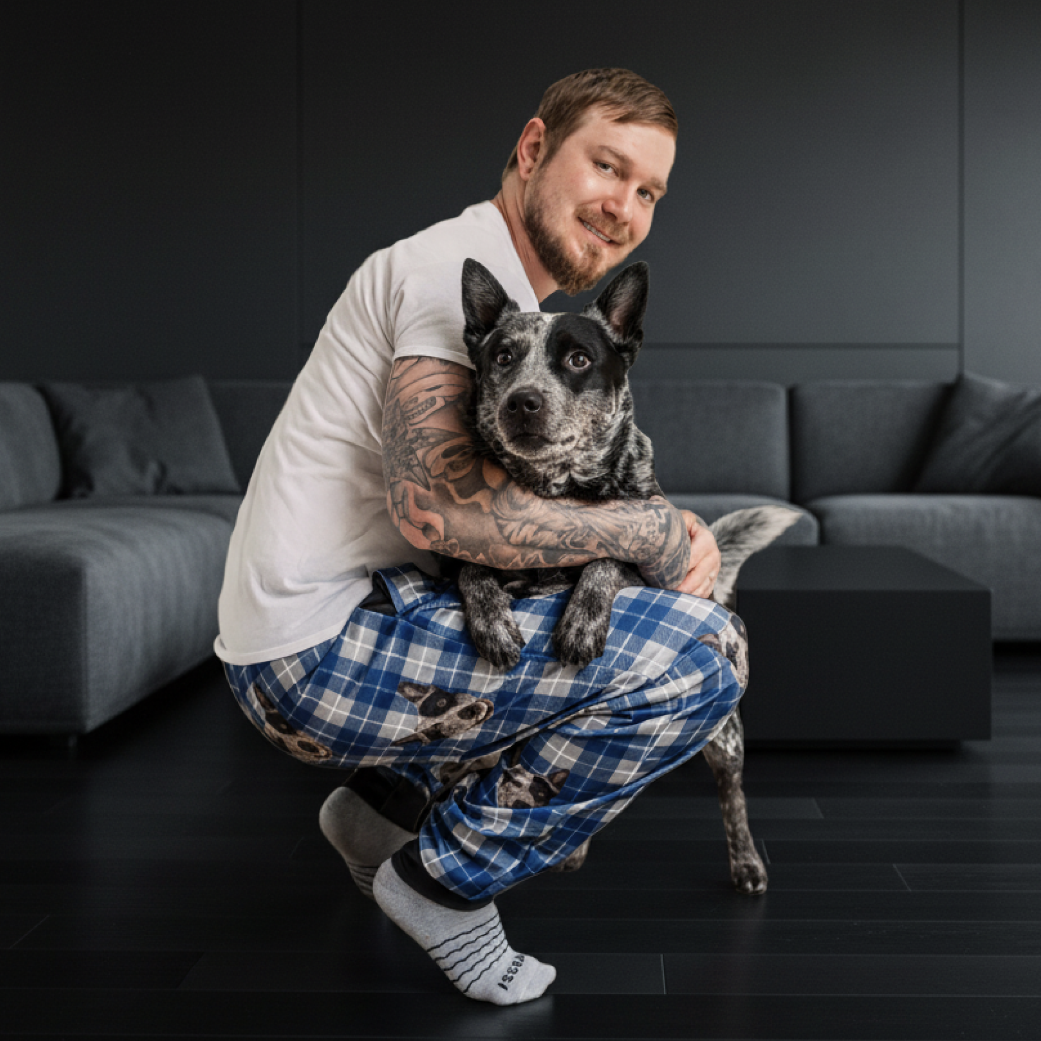 Person in plaid pajamas hugging a black and white dog on a living room.