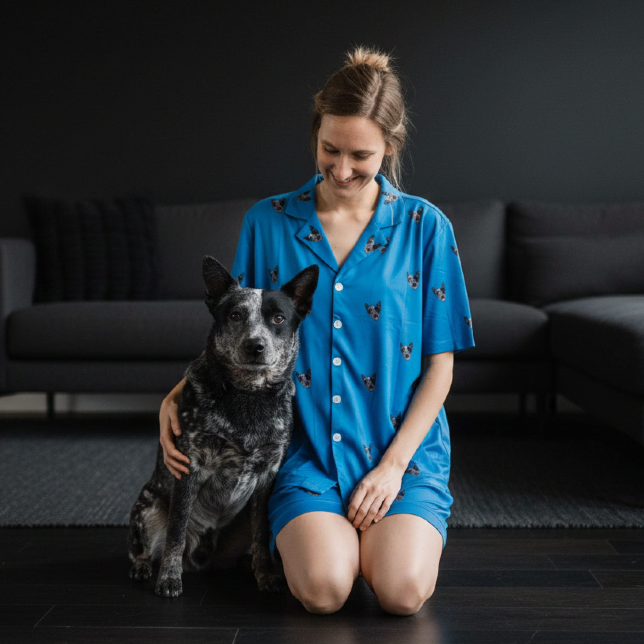 Woman in a blue button-down dog-print pajama set kneeling with a cattle dog.