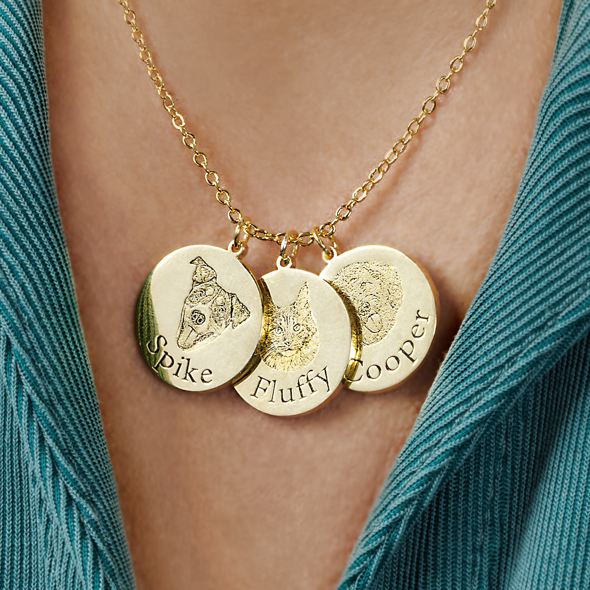 Close-up of a gold necklace with three engraved circular pendants, each featuring a pet's face and name: Spike with a dog, Fluffy with a cat, and Cooper with another dog.