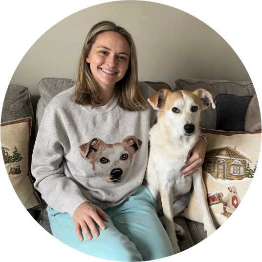 Person sitting on a couch with a dog, wearing a knit weater with a dog's face on it.