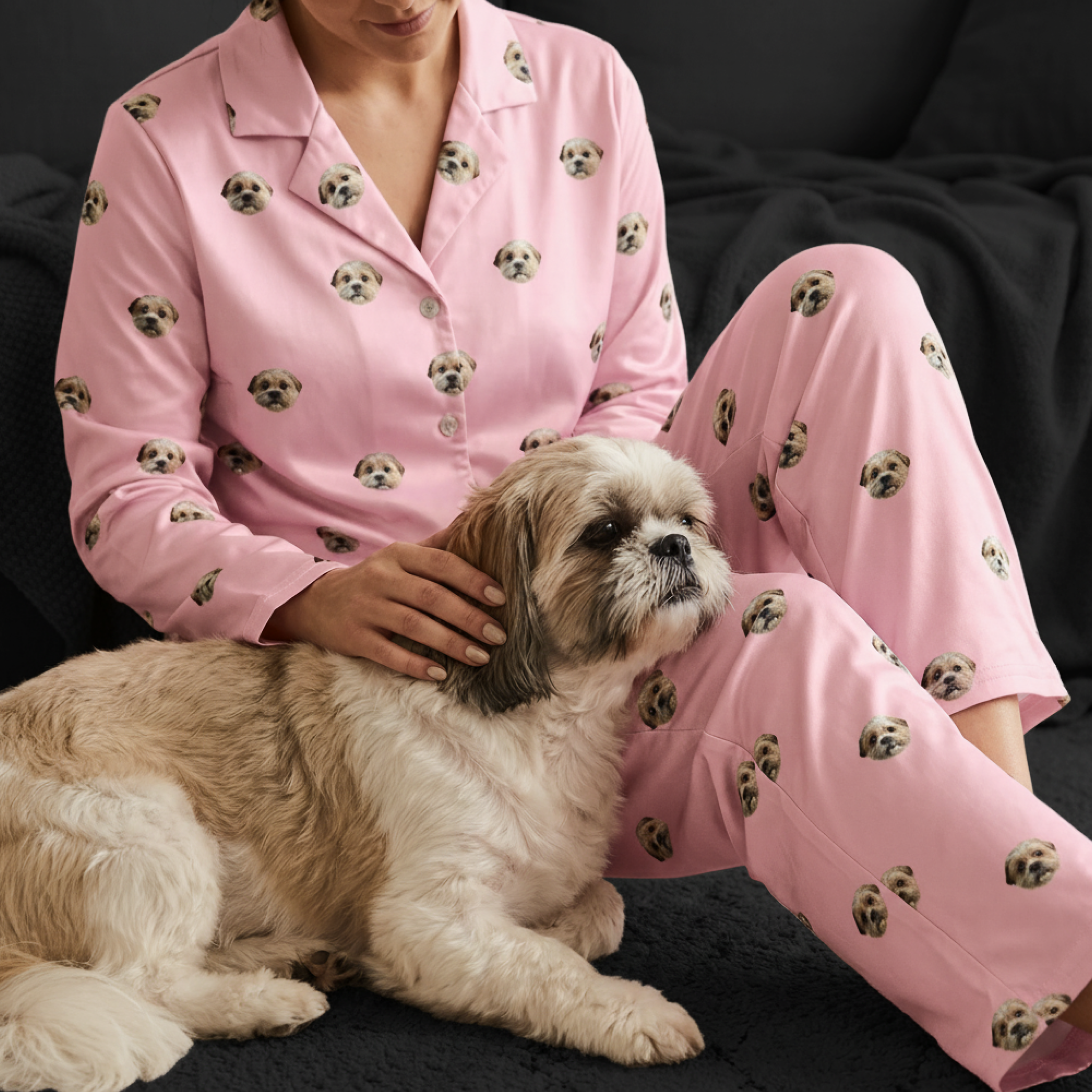 A person wearing pink pajamas printed with a dog's face pets a small, fluffy dog.