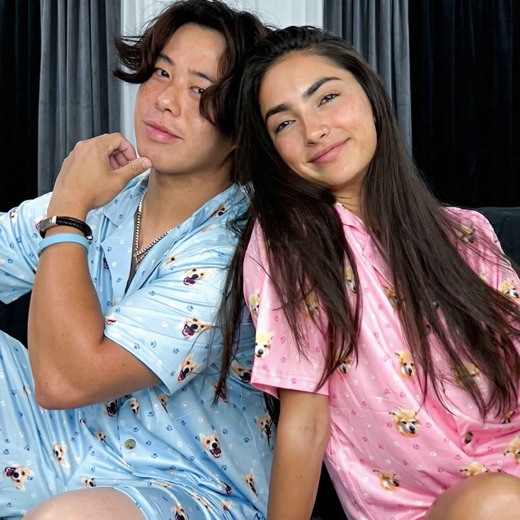 Man and woman sitting back-to-back on white rug wearing blue and pink Corgi-print pajamas