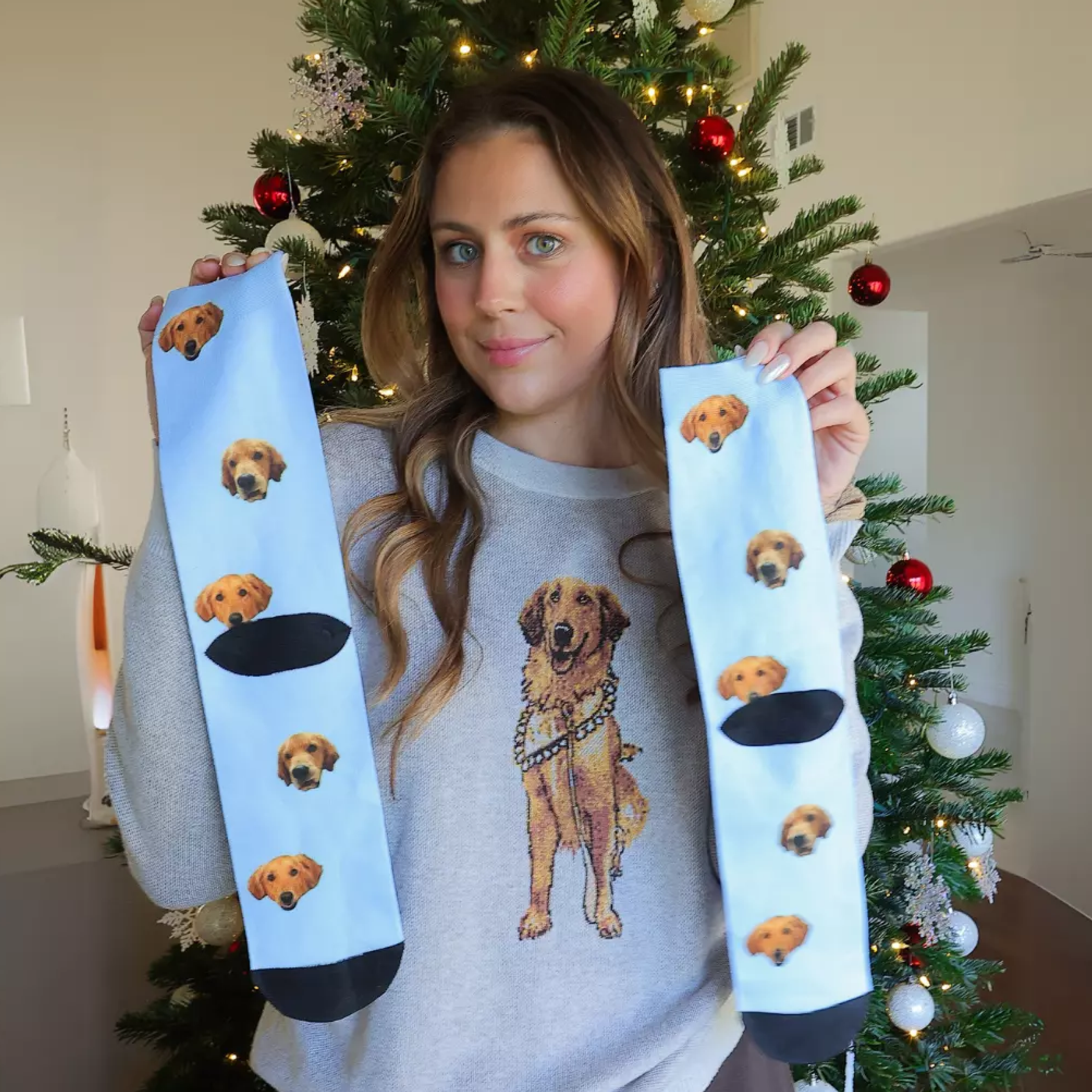 Person holding socks with dog faces, standing near a Christmas tree.