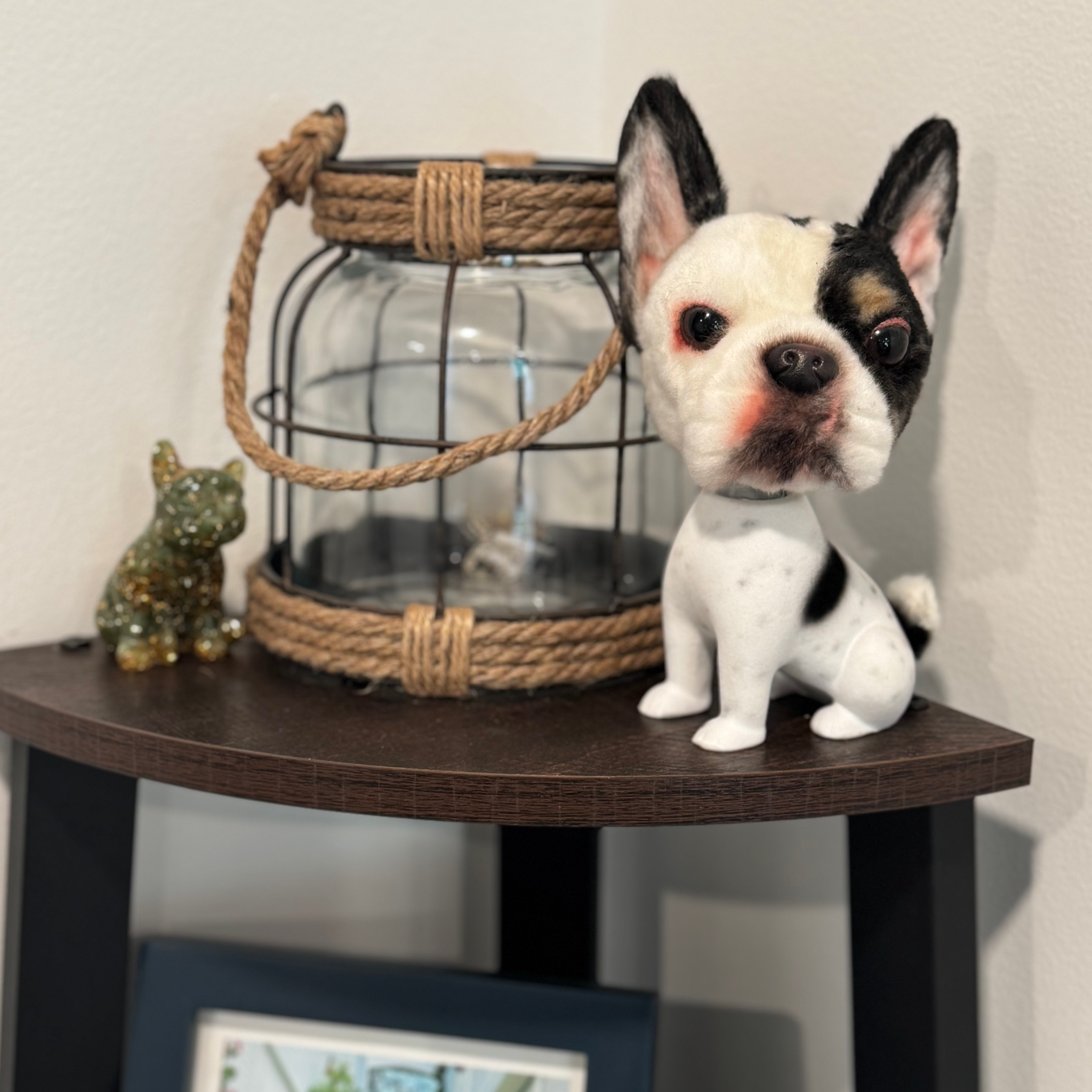 Black and white French Bulldog bobblehead on dark shelf with lantern and framed photo.