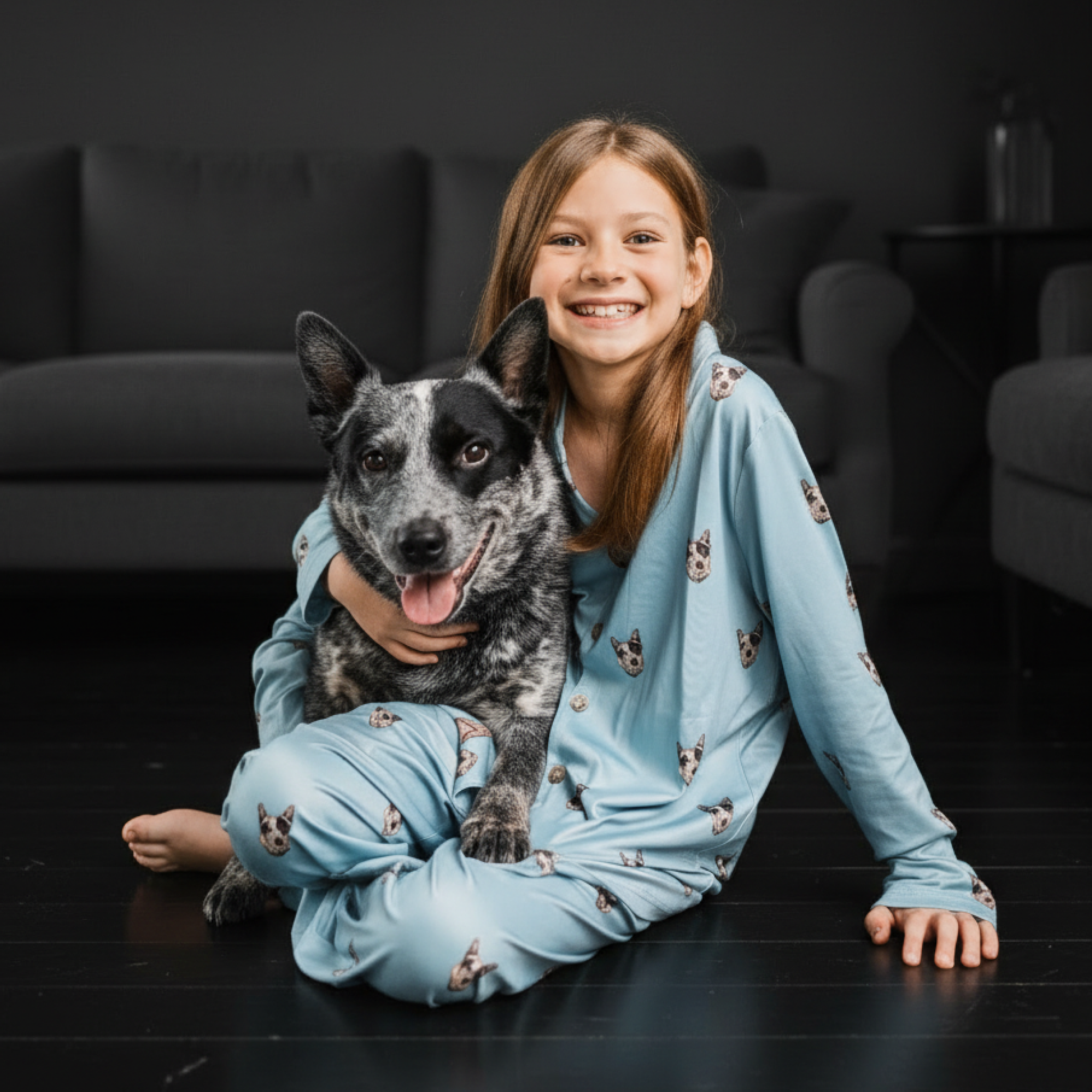 Girl in light blue dog-print button-down pajamas hugging a cattle dog.