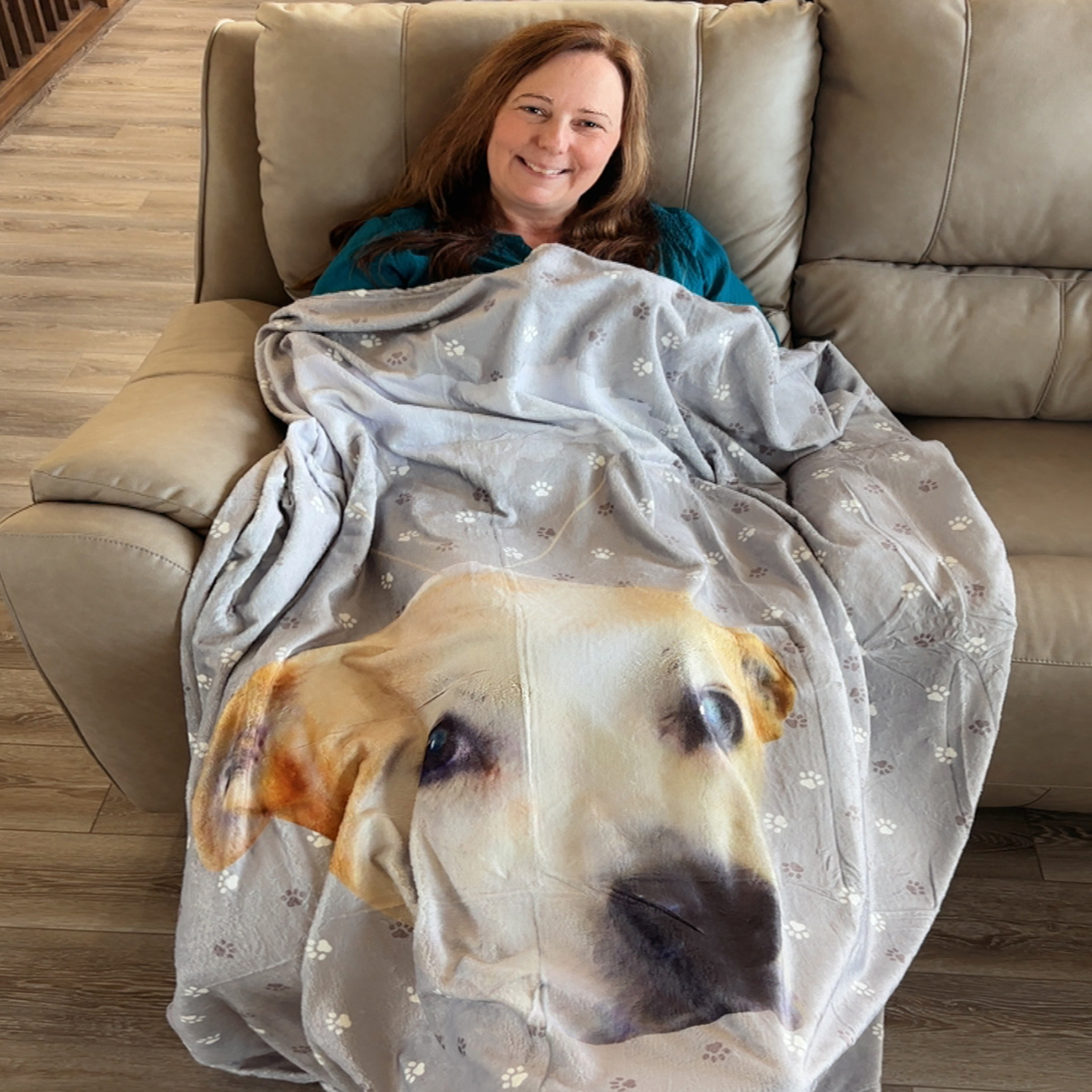 A woman wraps herself in a cozy blanket printed with a large dog portrait while sitting indoors.