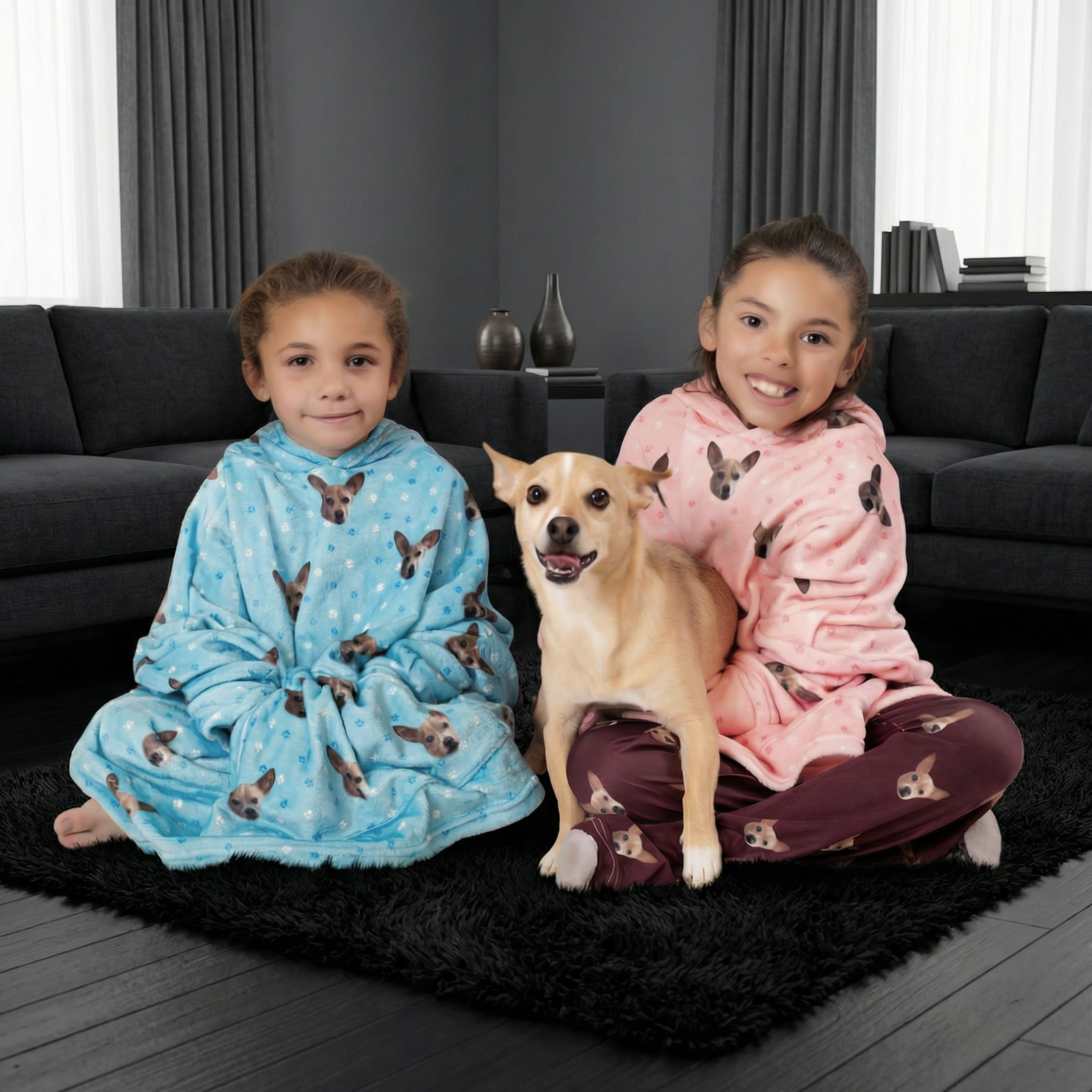 Two girls in blue and pink dog-print oversized hoodies sitting with a tan dog