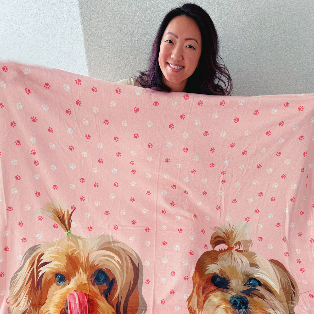A person holds out a colorful blanket featuring two pet faces.