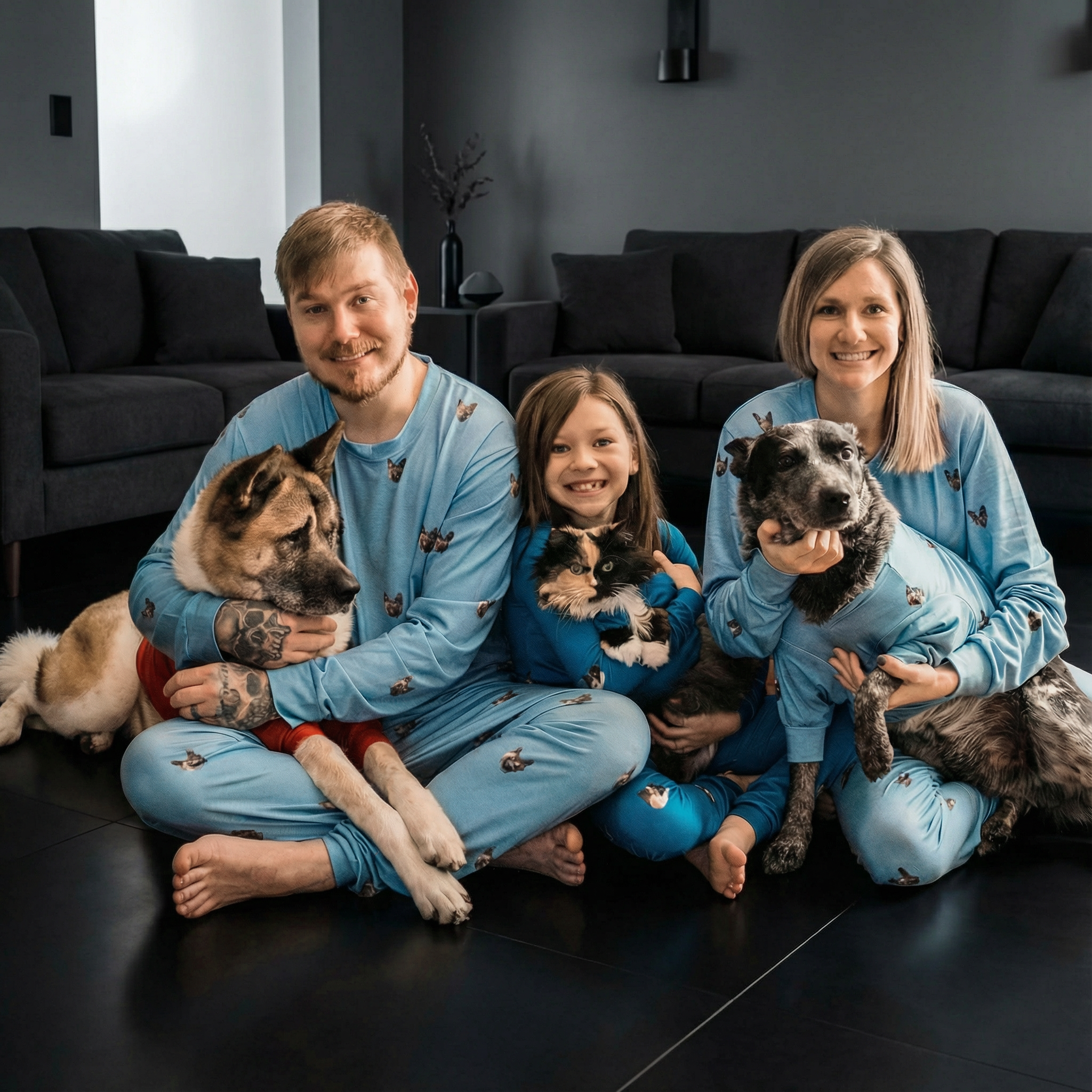 A family of three and two dogs wearing matching light blue pajamas in a dark living room.