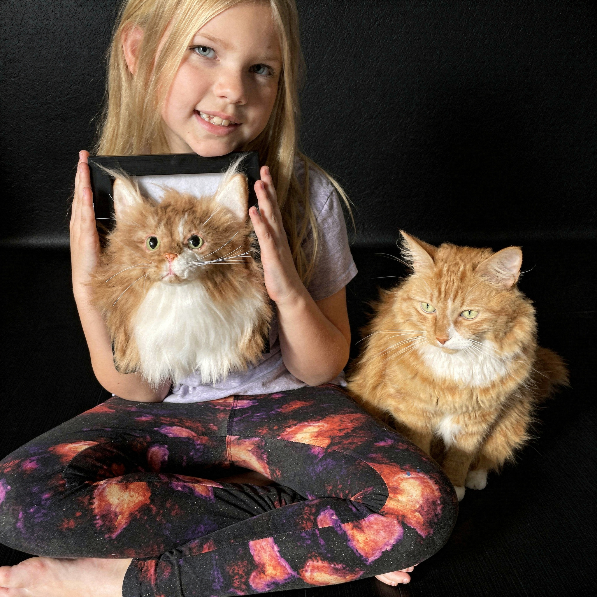 Young girl holding a framed custom portrait of her orange and white long-haired cat indoors.