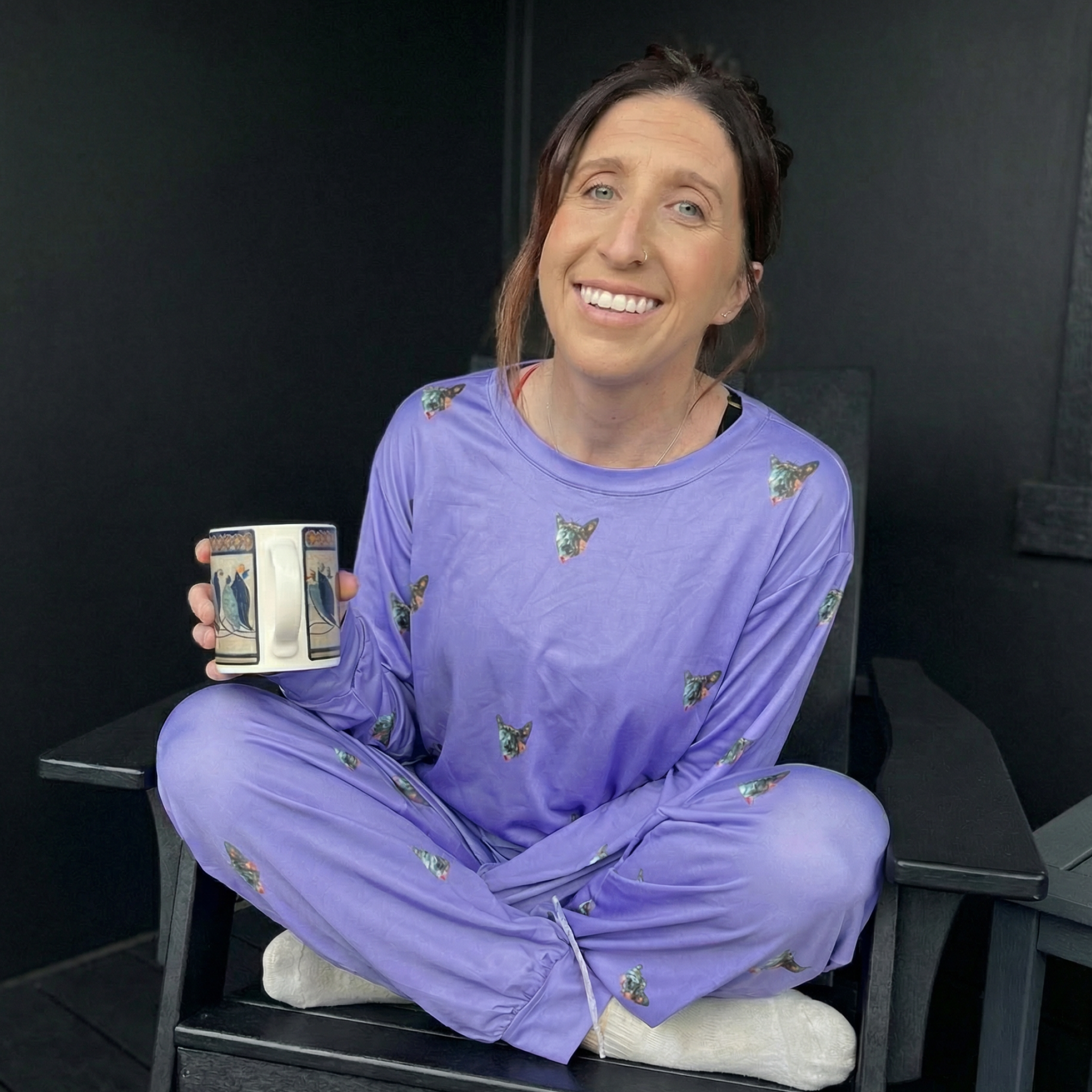 Person in purple pajamas sitting cross-legged, holding a coffee mug indoors.