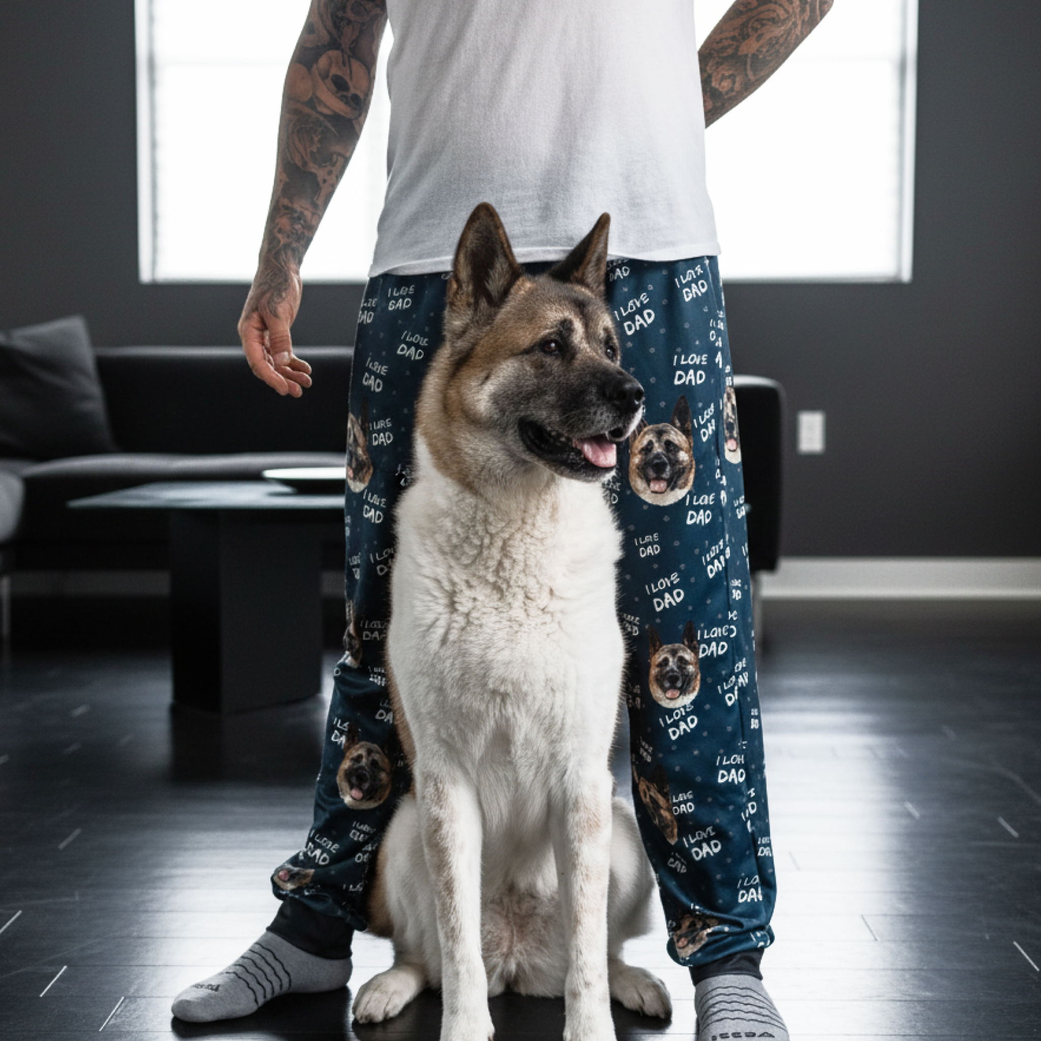 In a living room, a person wears Akita pajamas patterned with “I LOVE DAD” and a dog.