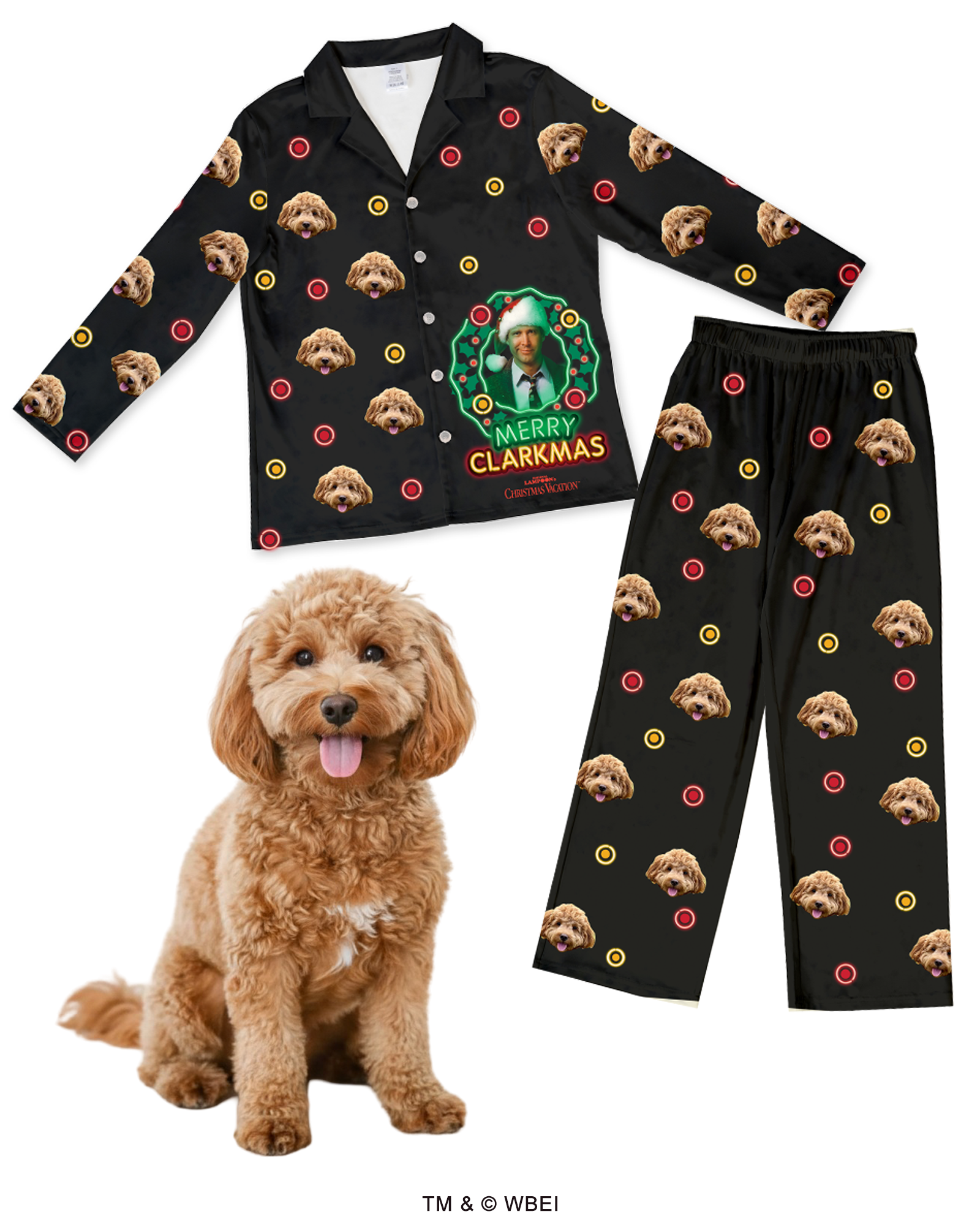 A black pajama set (long-sleeve collared top and pants) featuring a central graphic of Clark Griswold inside a green Christmas wreath on the top, with the text 'MERRY CLARKMAS.' The entire set is patterned with a repeating design of a fluffy brown Cockapoo's face and small red and yellow circles (like ornaments). A real Cockapoo dog sits in the foreground.