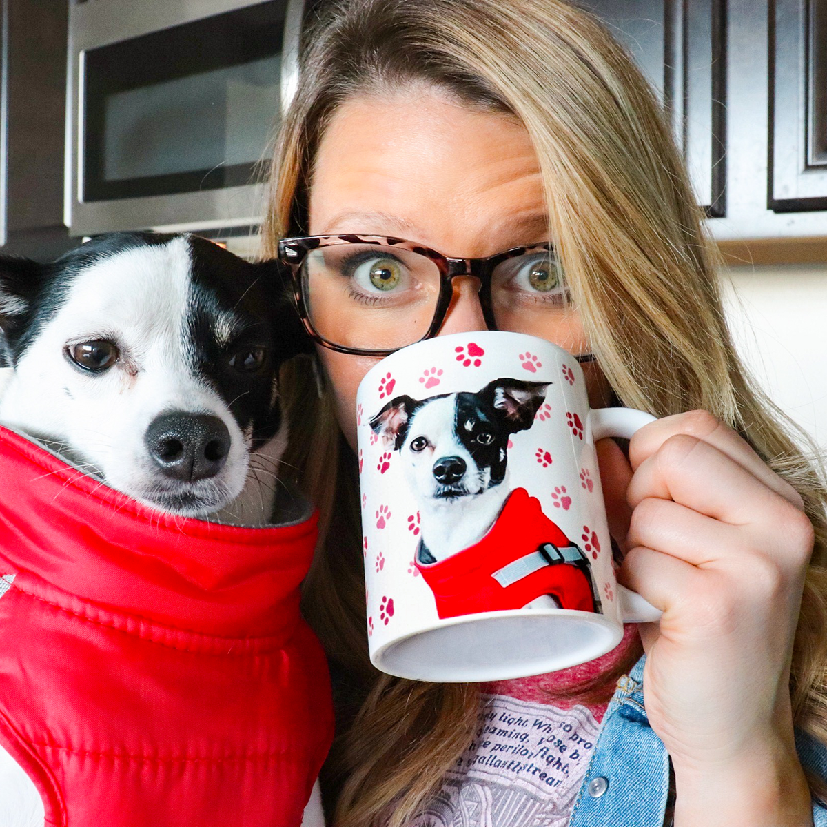 A close-up of a smiling woman with long blonde hair and glasses, holding a white mug up to her face.