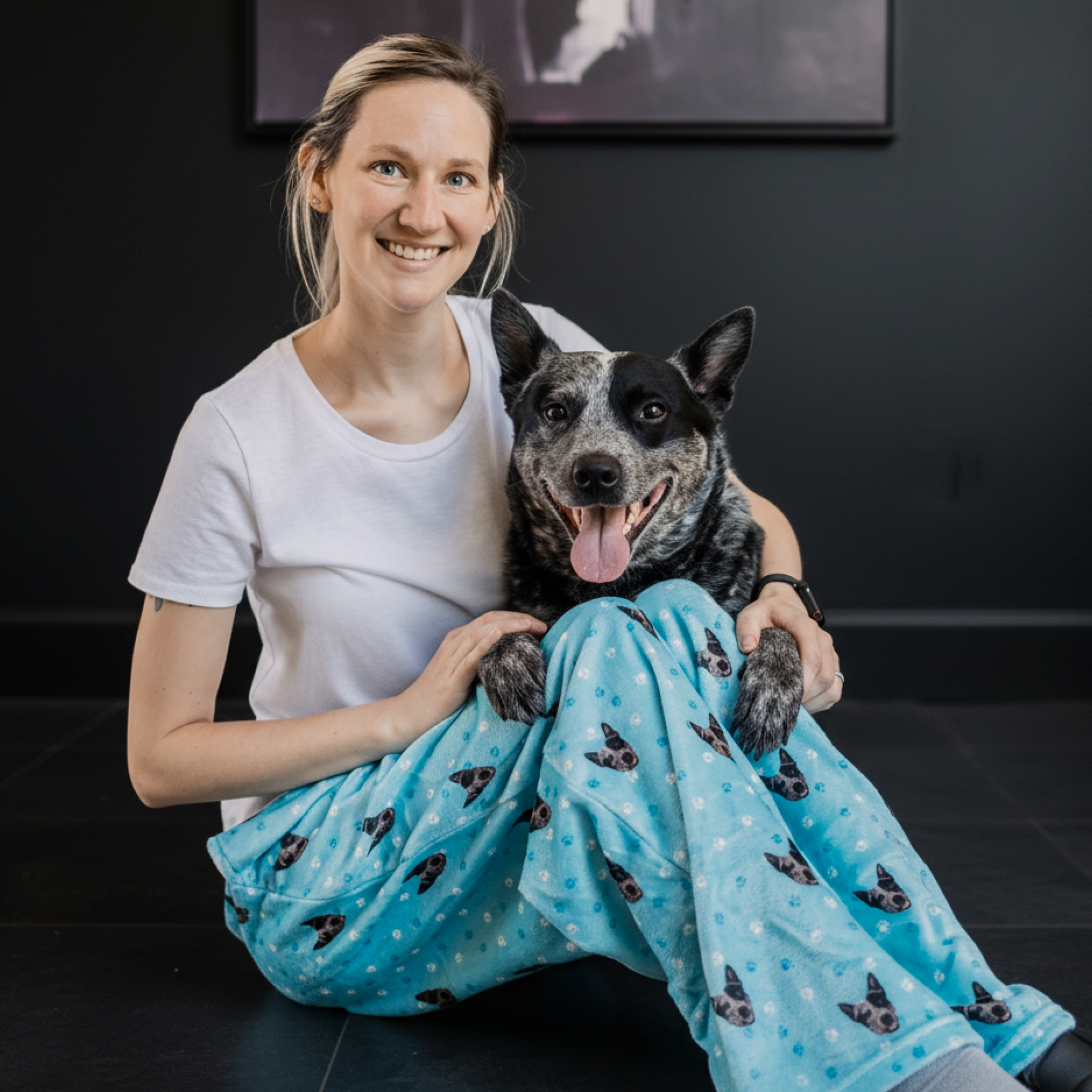 Woman sitting on ground with black and white dog, both wearing dog-print fleece pajama pants