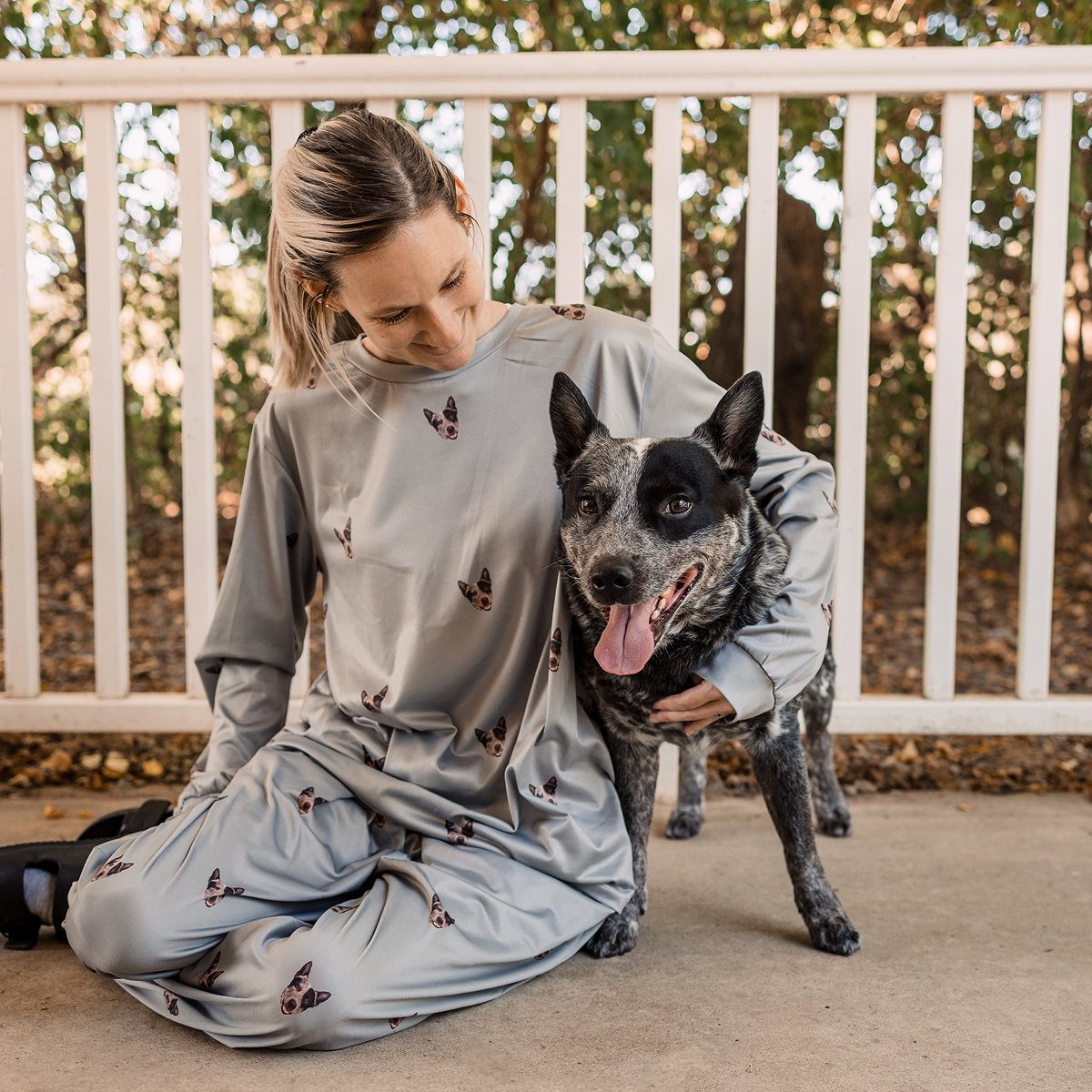 Person sitting on a porch next to a black and white dog, smiling.