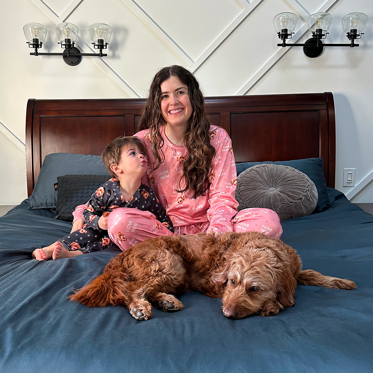 Woman and child in pajamas sitting on bed with a dog.