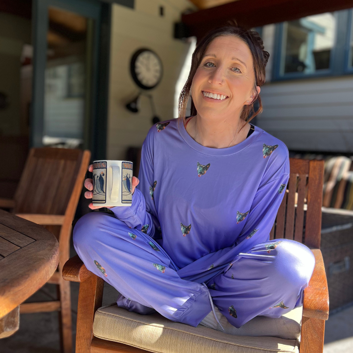 Person in purple pajamas sitting cross-legged, holding a coffee mug indoors.