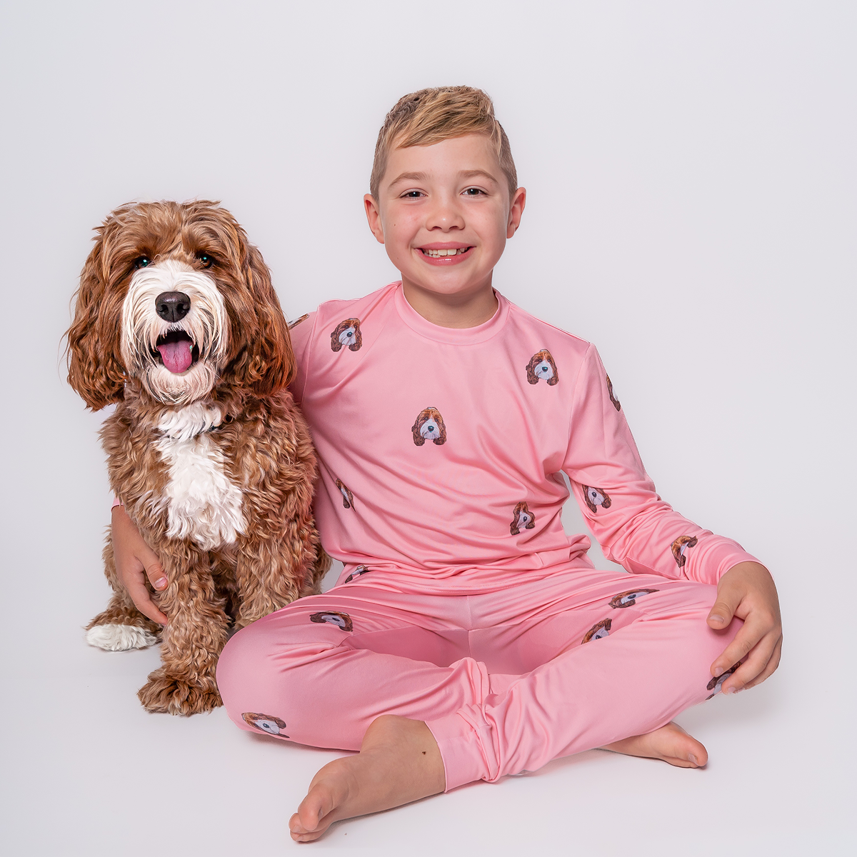 Child in pink pajamas sitting with a curly-haired dog.