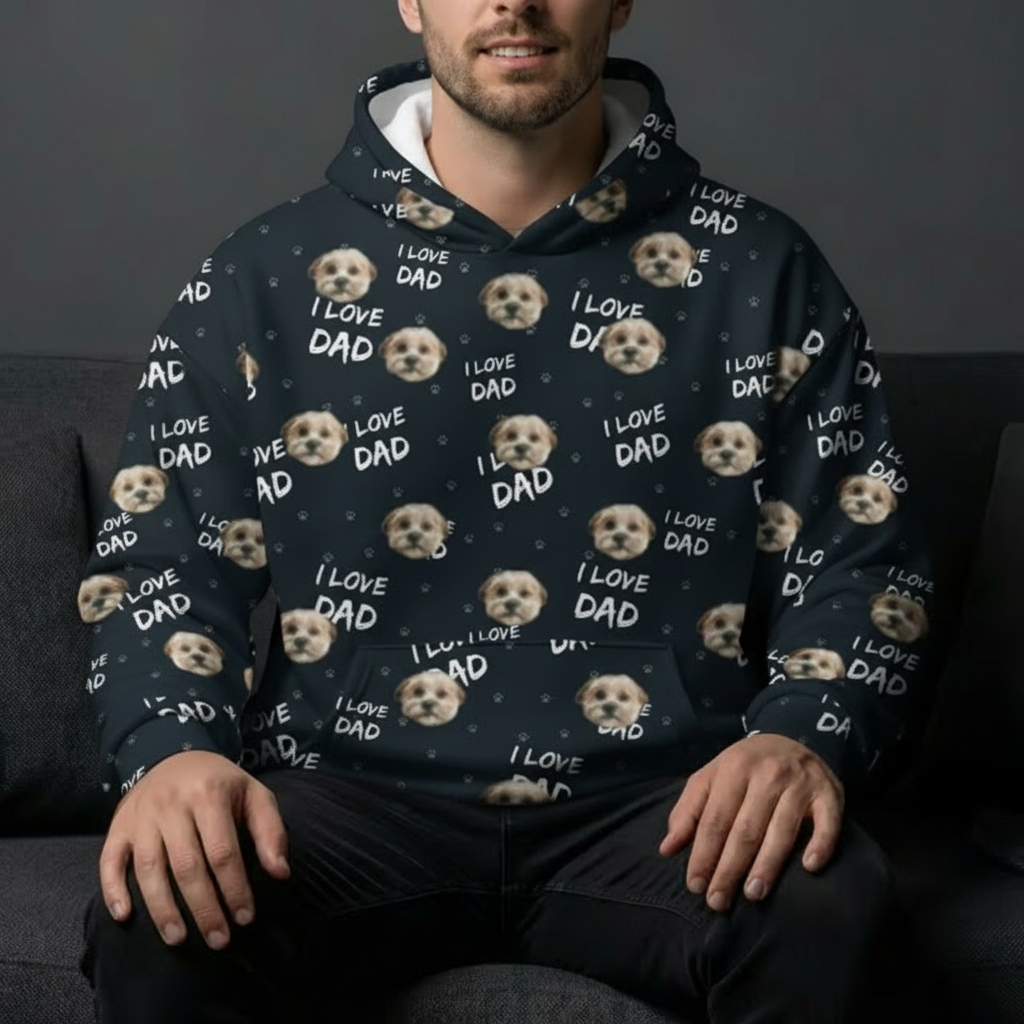 A man sitting on a sofa wearing a navy blue hoodie covered in a repeating pattern of a small dog's face and the text 'I LOVE DAD' in white lettering.