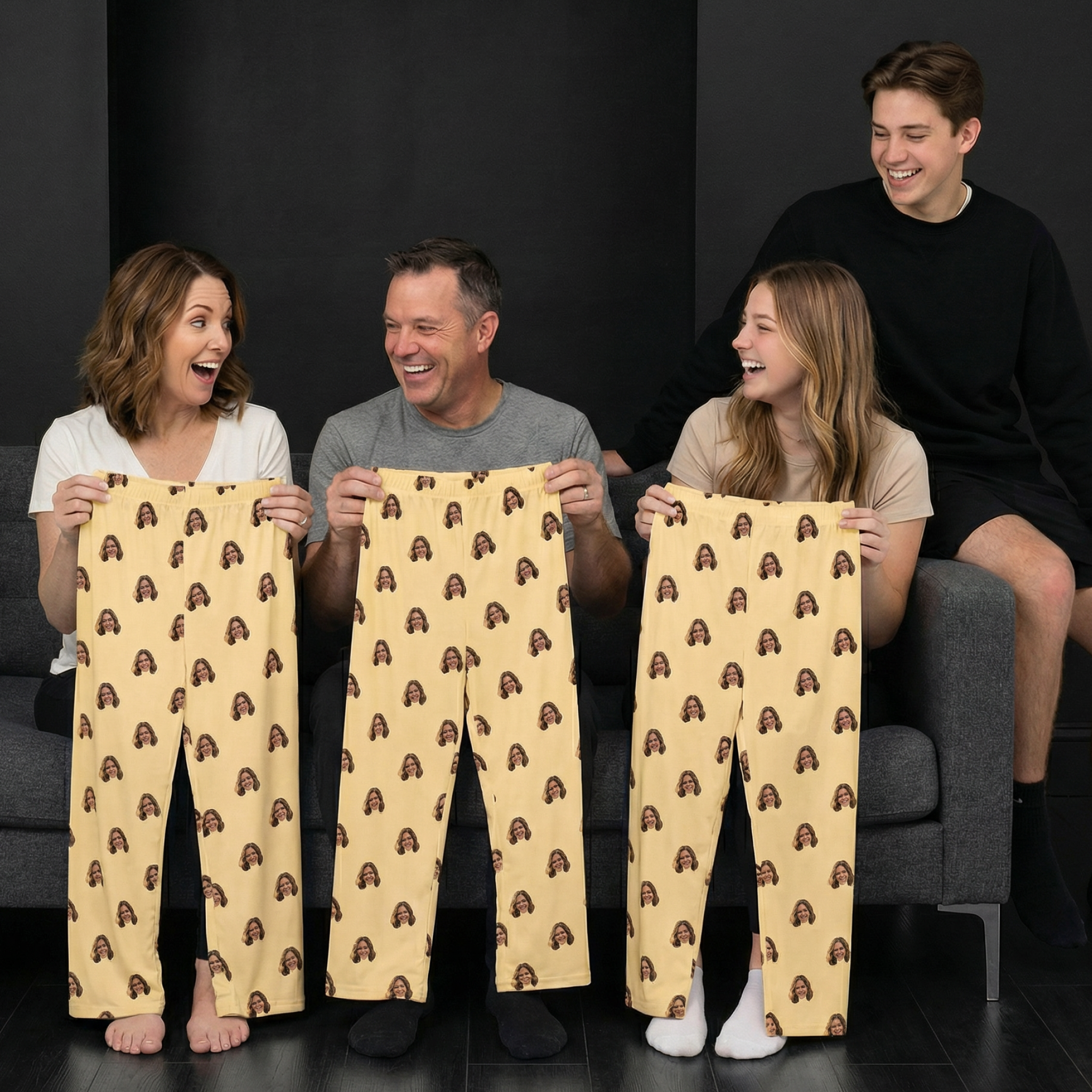 A family laughs while holding up pajama pants printed with a woman's face on them.
