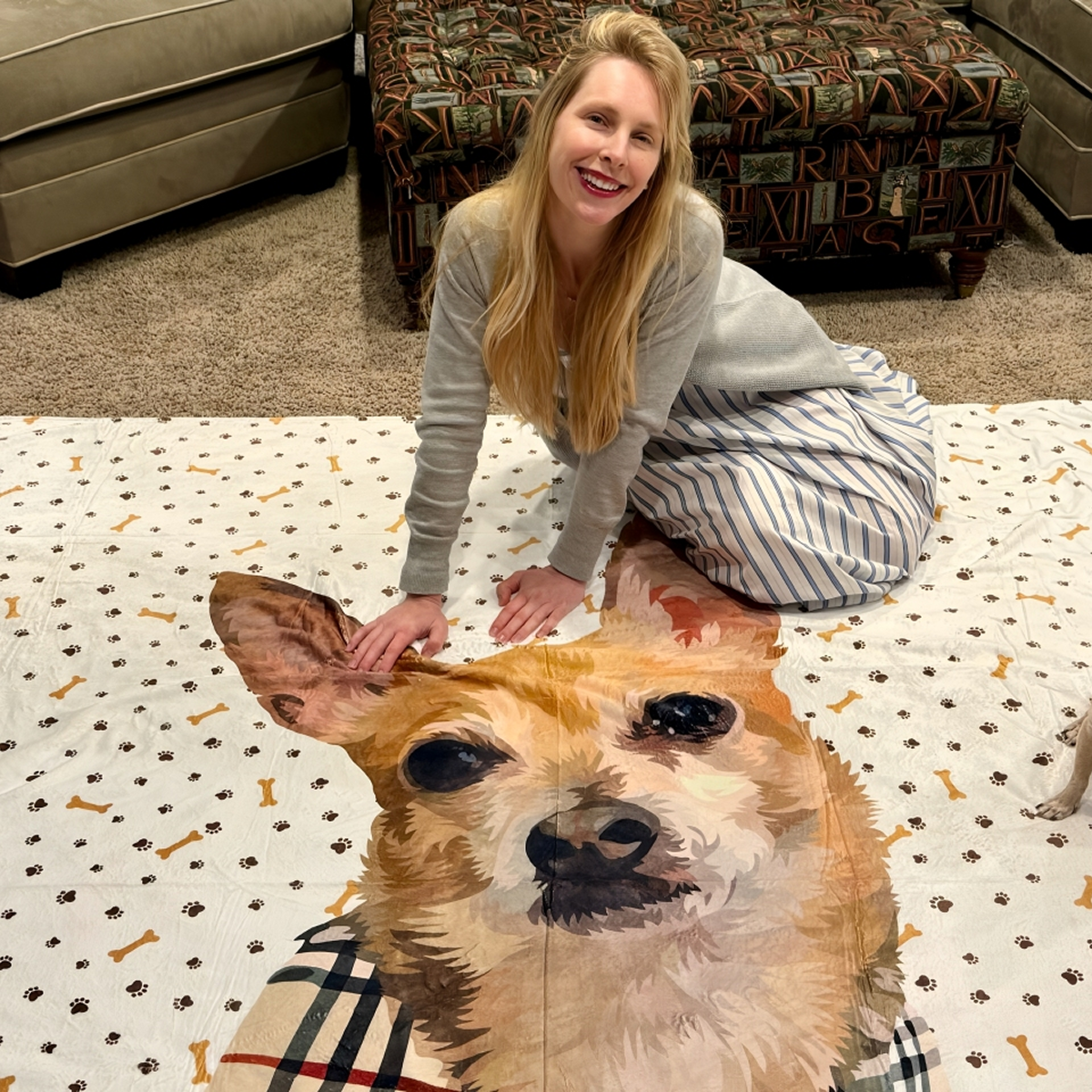 A woman smiles while holding up a blanket decorated with a realistic portrait of her dog.