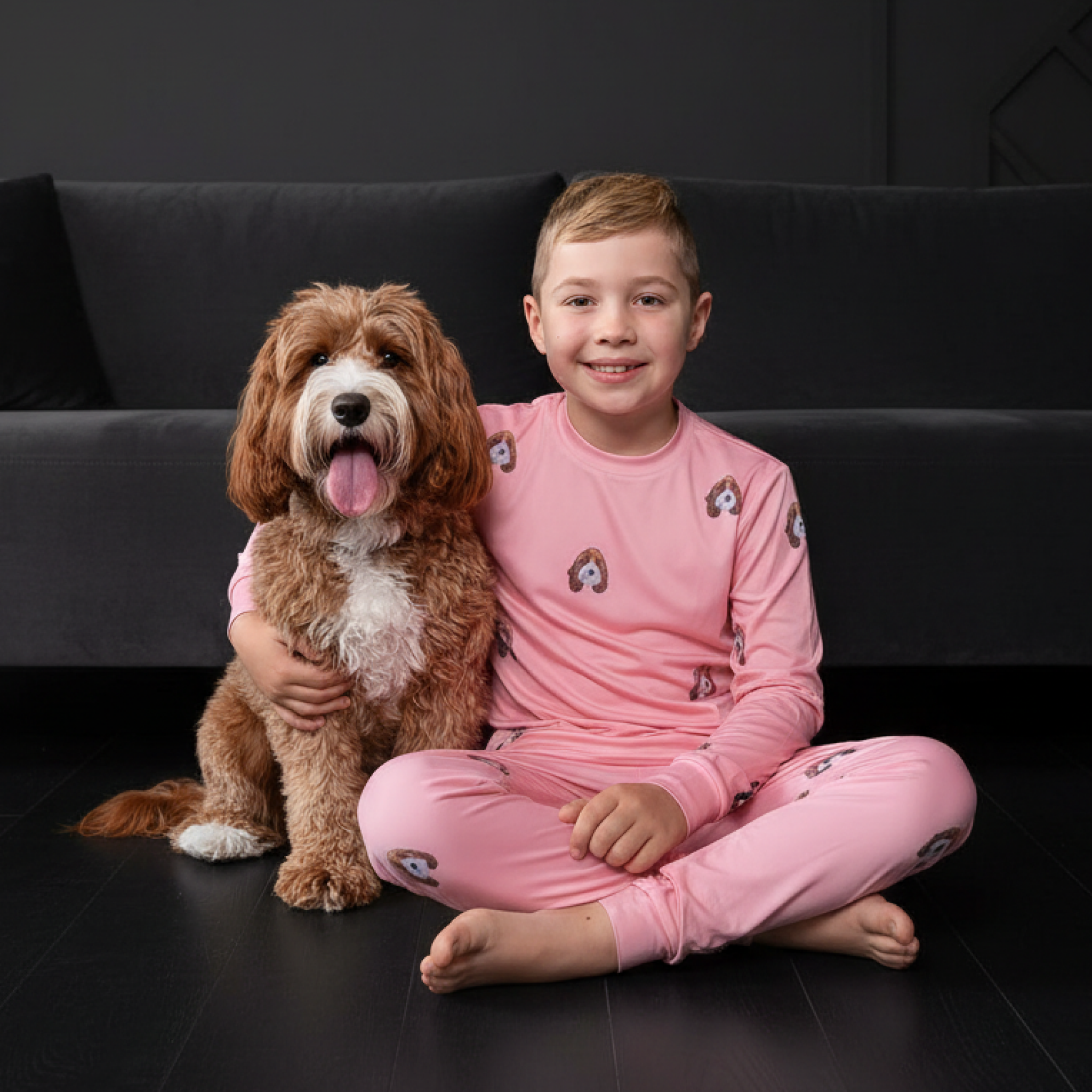 Boy in pink dog-print pajamas sitting on the floor with a fluffy brown dog