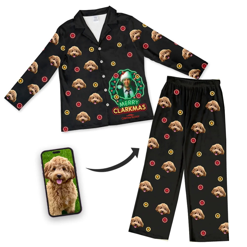 A black pajama set (long-sleeve collared top and pants) features a central graphic of Clark Griswold inside a green Christmas wreath on the top, with the text 'MERRY CLARKMAS.' The entire set is patterned with a repeating design of a fluffy brown Cockapoo's face and small red and yellow circles (like ornaments). A smartphone screen inset shows the original photo of the Cockapoo, with an arrow pointing to the pajamas.