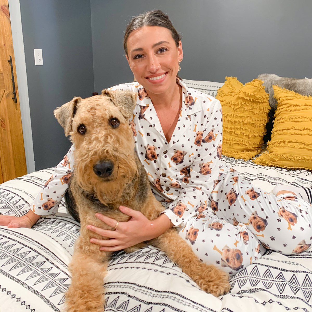 Person in dog-themed pajamas sitting on a bed with a large, fluffy dog.
