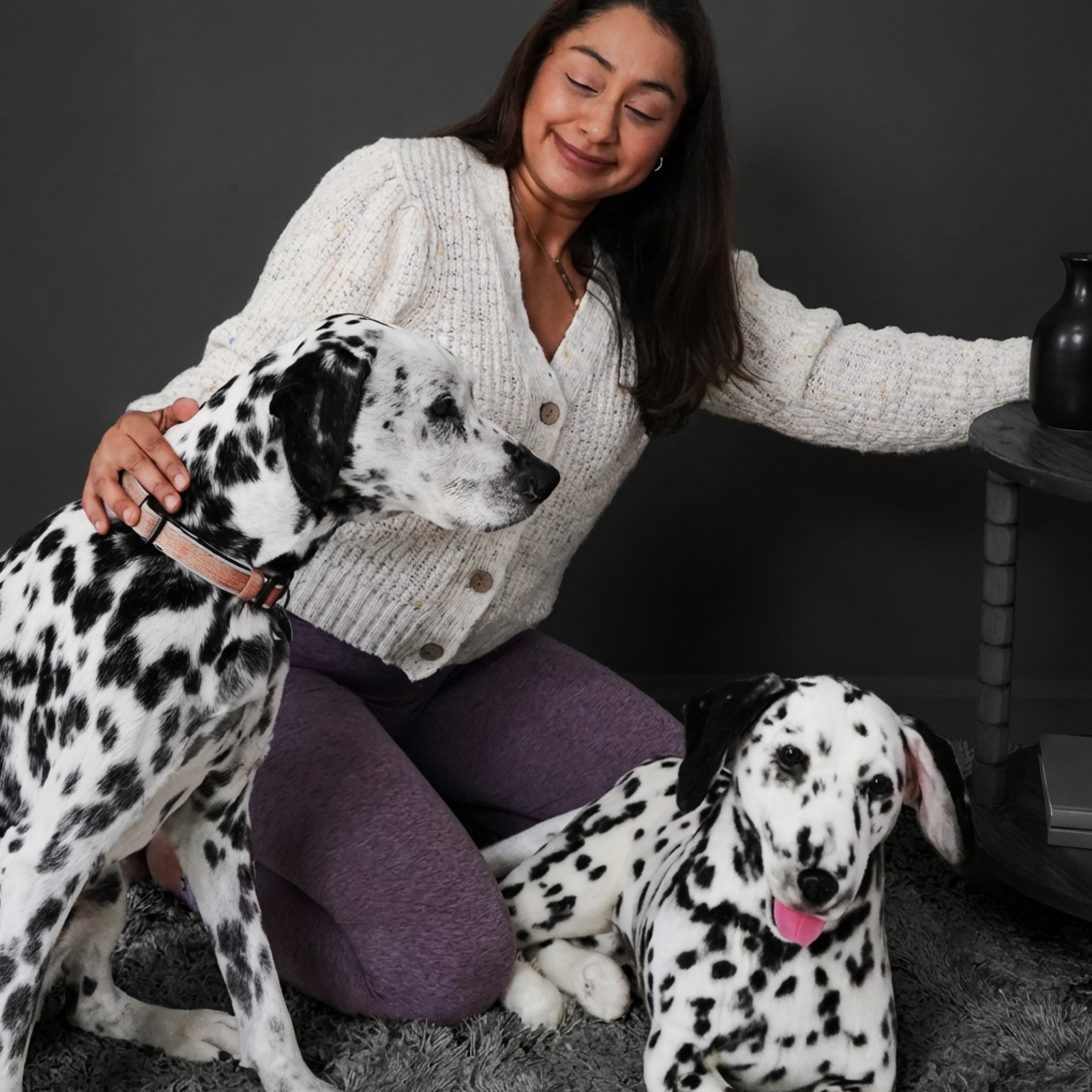 Woman smiles on floor with real & plush Dalmatians in cozy living room.