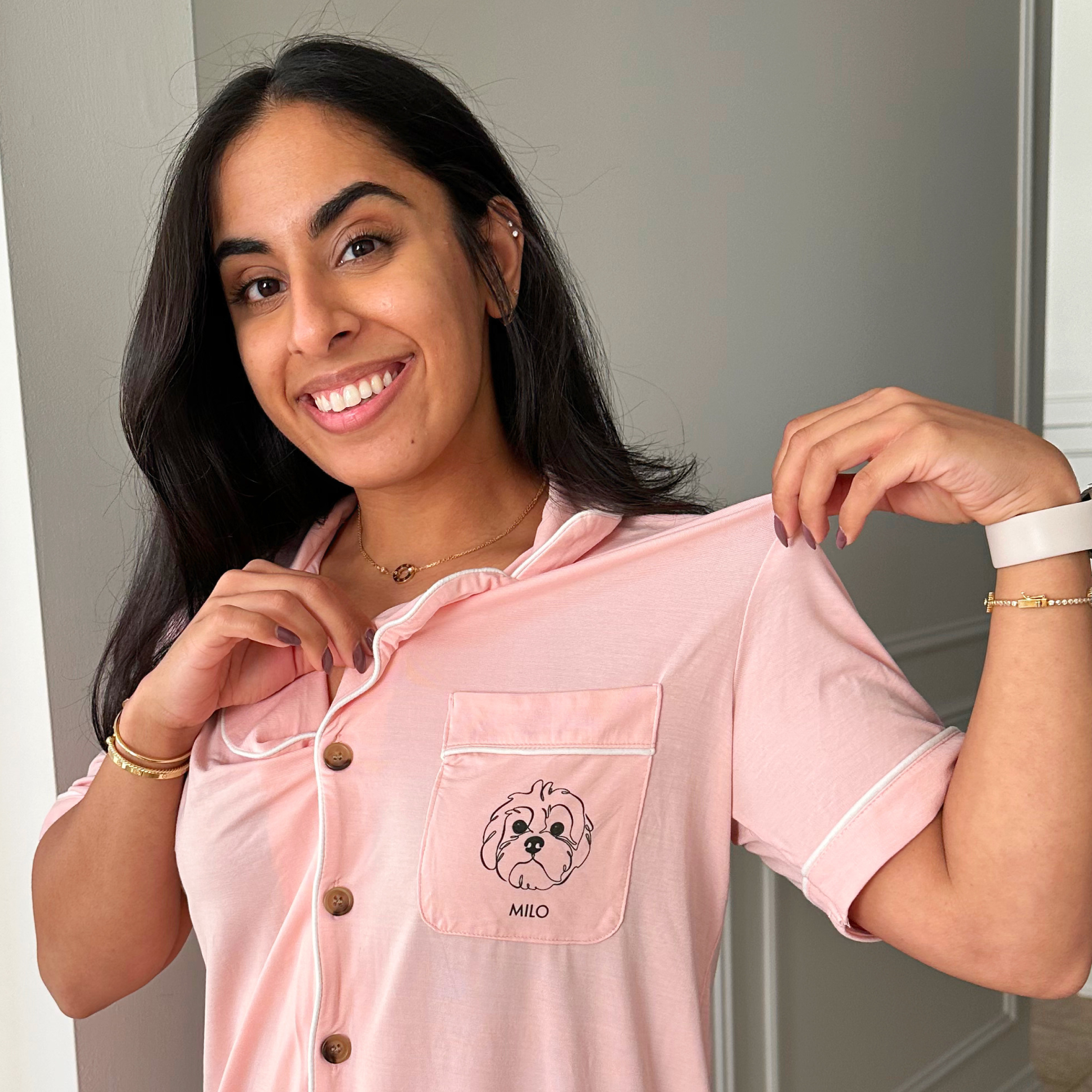 Person smiling, holding the collar of a pink shirt with a dog illustration on the pocket.