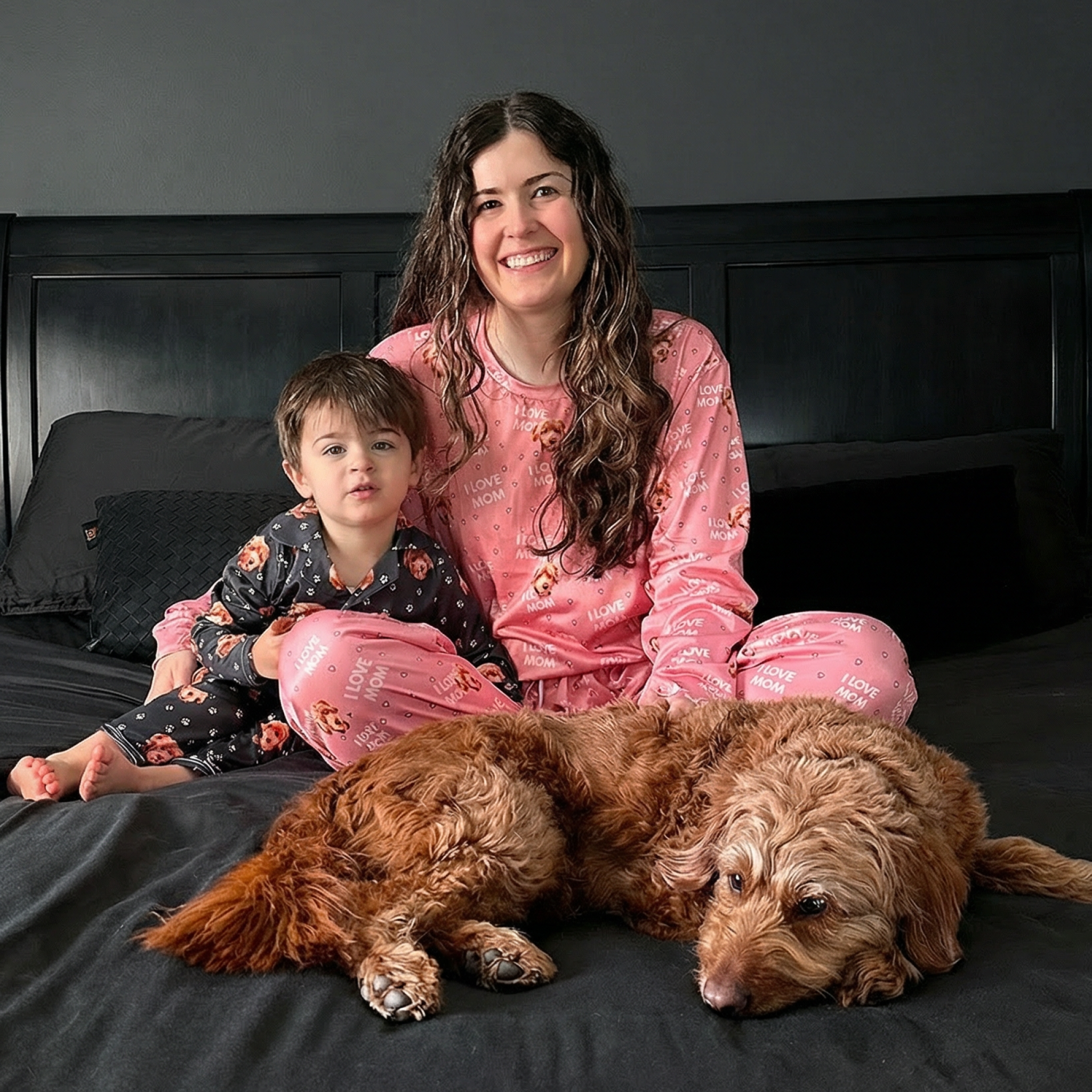 Woman and child in pajamas sitting on bed with a dog.