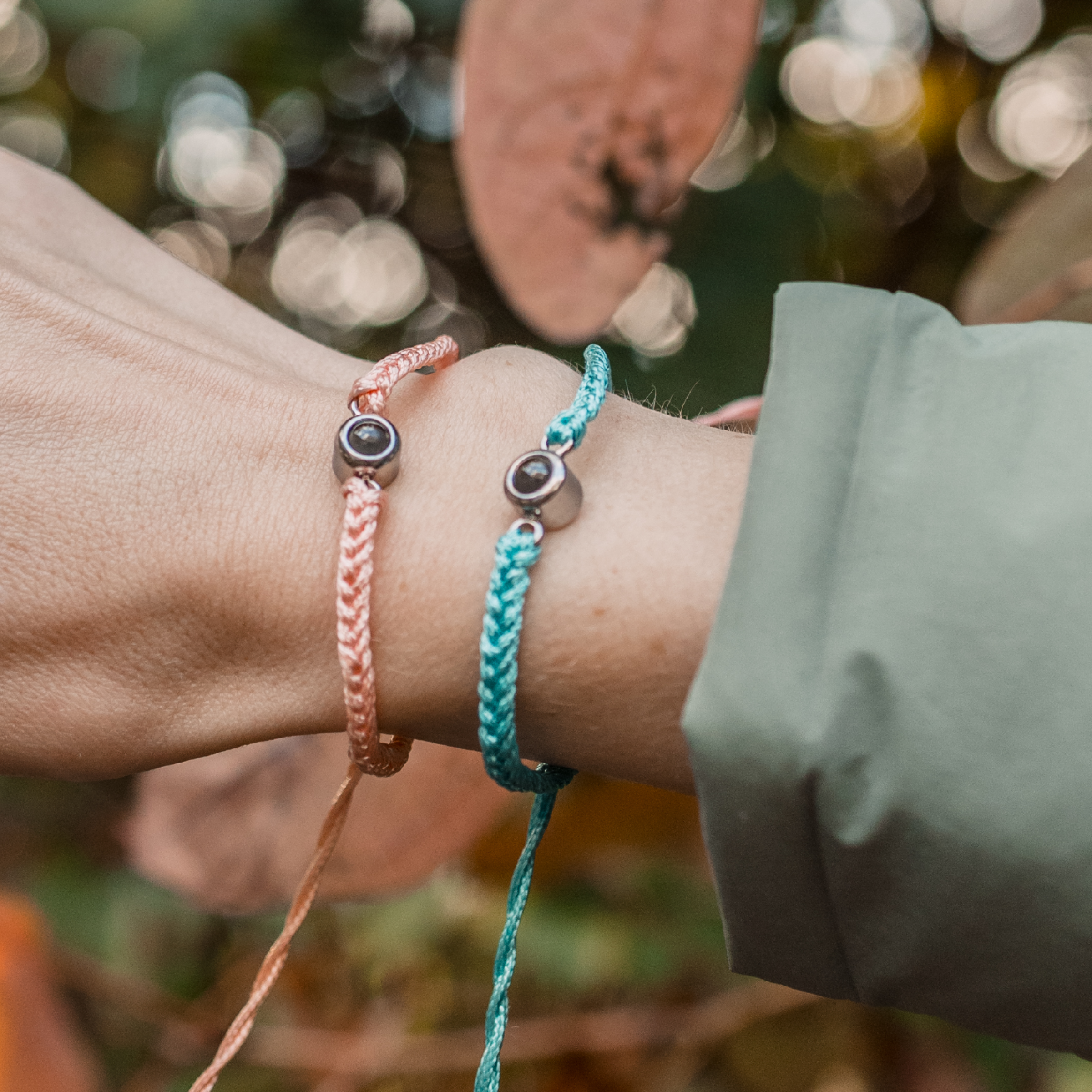 One arm wearing two woven cord bracelets. One bracelet is peach/pink and the other is teal/turquoise.  
