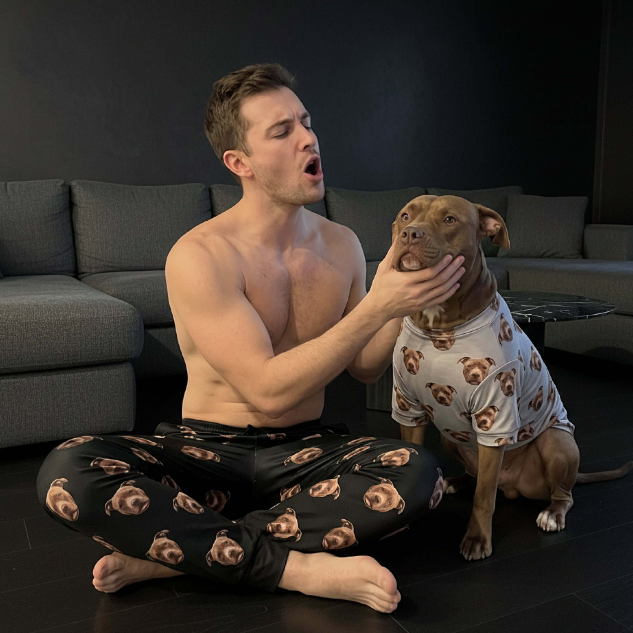 A shirtless man and a dog wear matching pajamas printed with the dog's face in a living room.