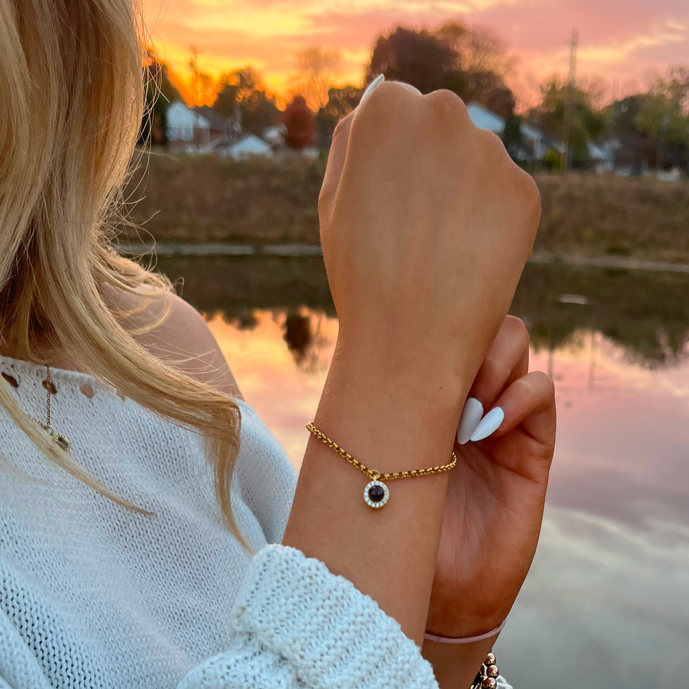 A close-up shot of a blonde woman wearing a white, off-the-shoulder sweater at sunset. 