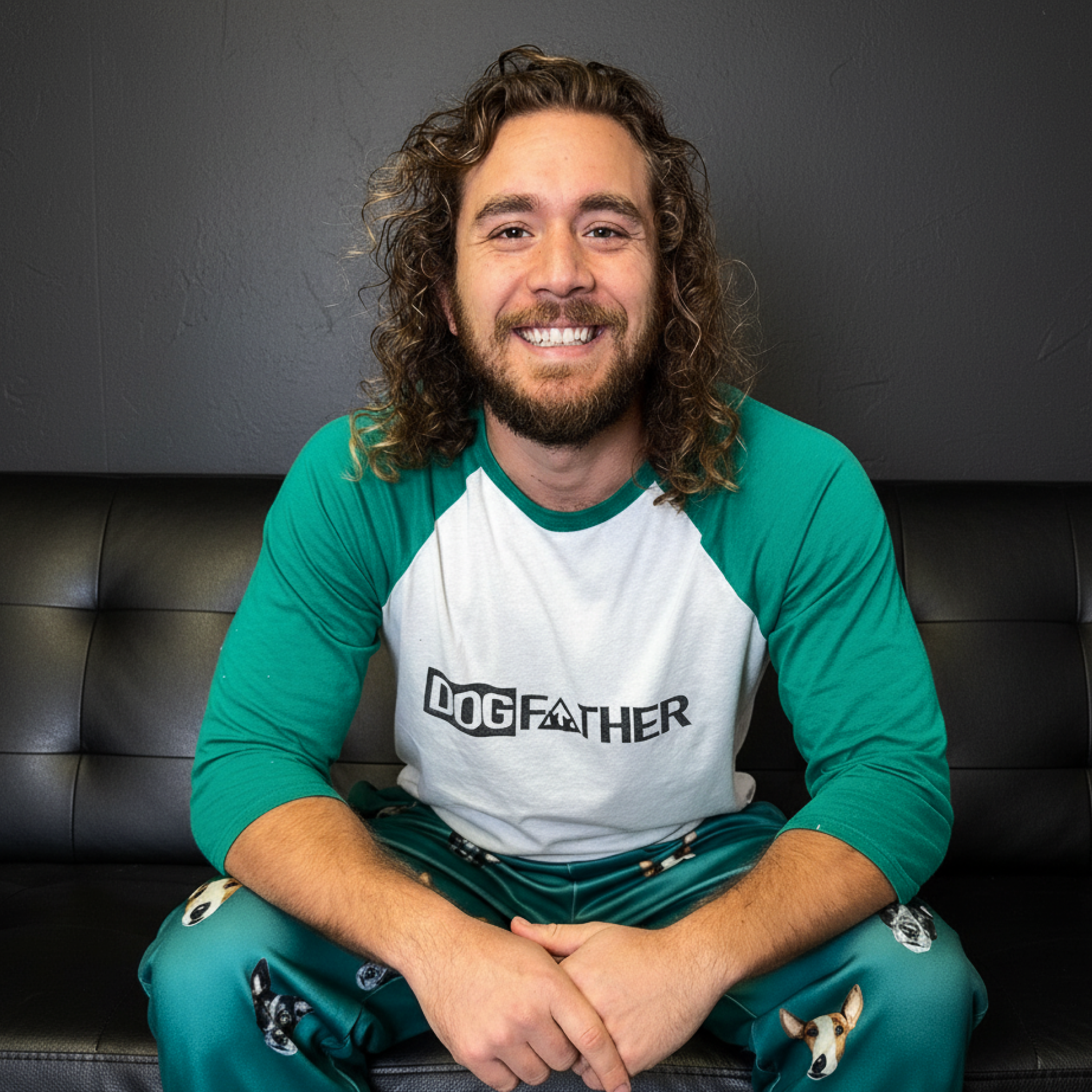 Smiling man in DOG FATHER shirt and terrier-face pajamas sits on a paw-print couch.