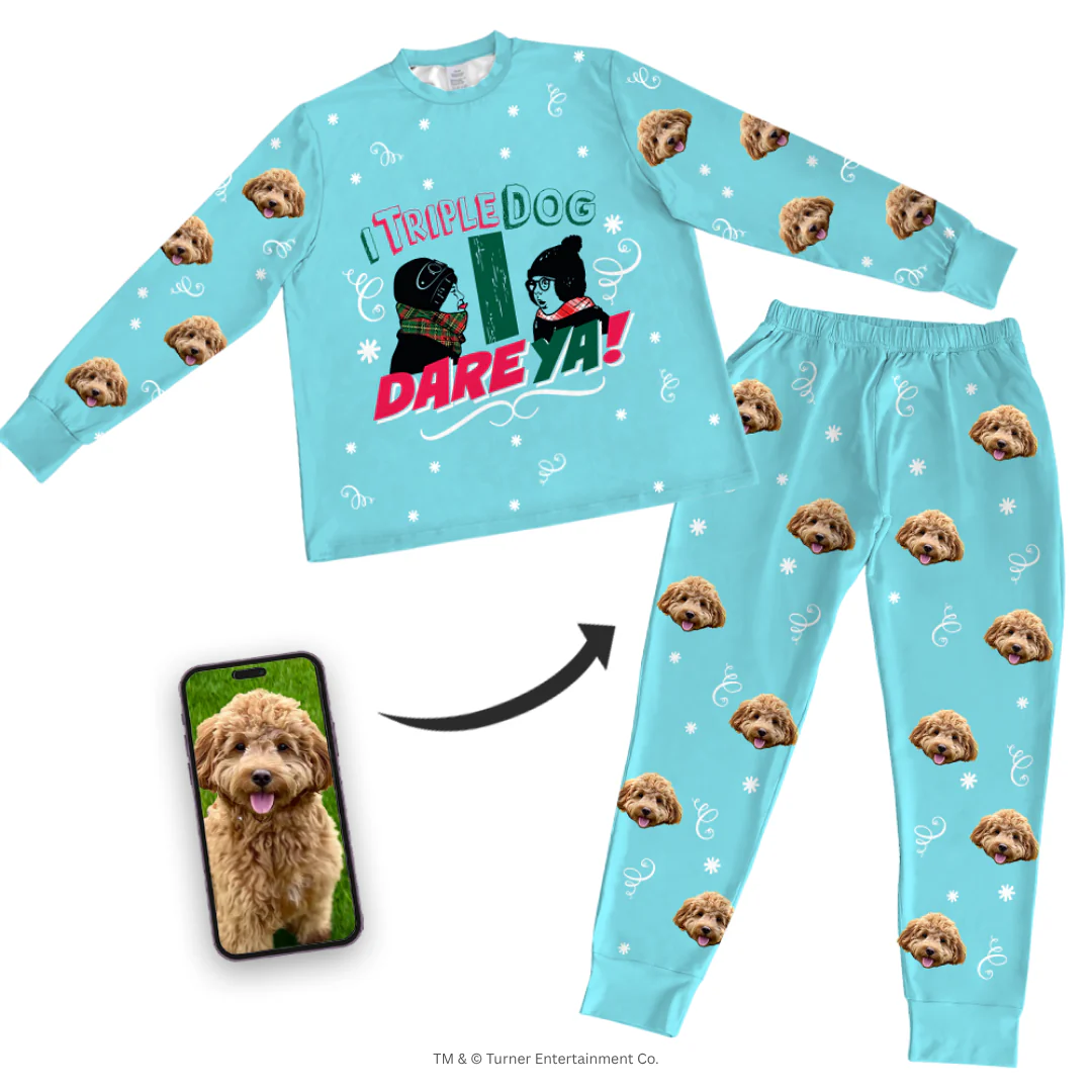 A light blue pajama set (long-sleeve top and pants) features a graphic of Flick and Schwartz and the quote 'I TRIPLE DOG DARE YA!' The set is patterned with white snowflakes, scrollwork, and a repeating design of a fluffy brown Cockapoo's face. A smartphone screen inset shows the original photo of the Cockapoo, with an arrow pointing to the pajamas.