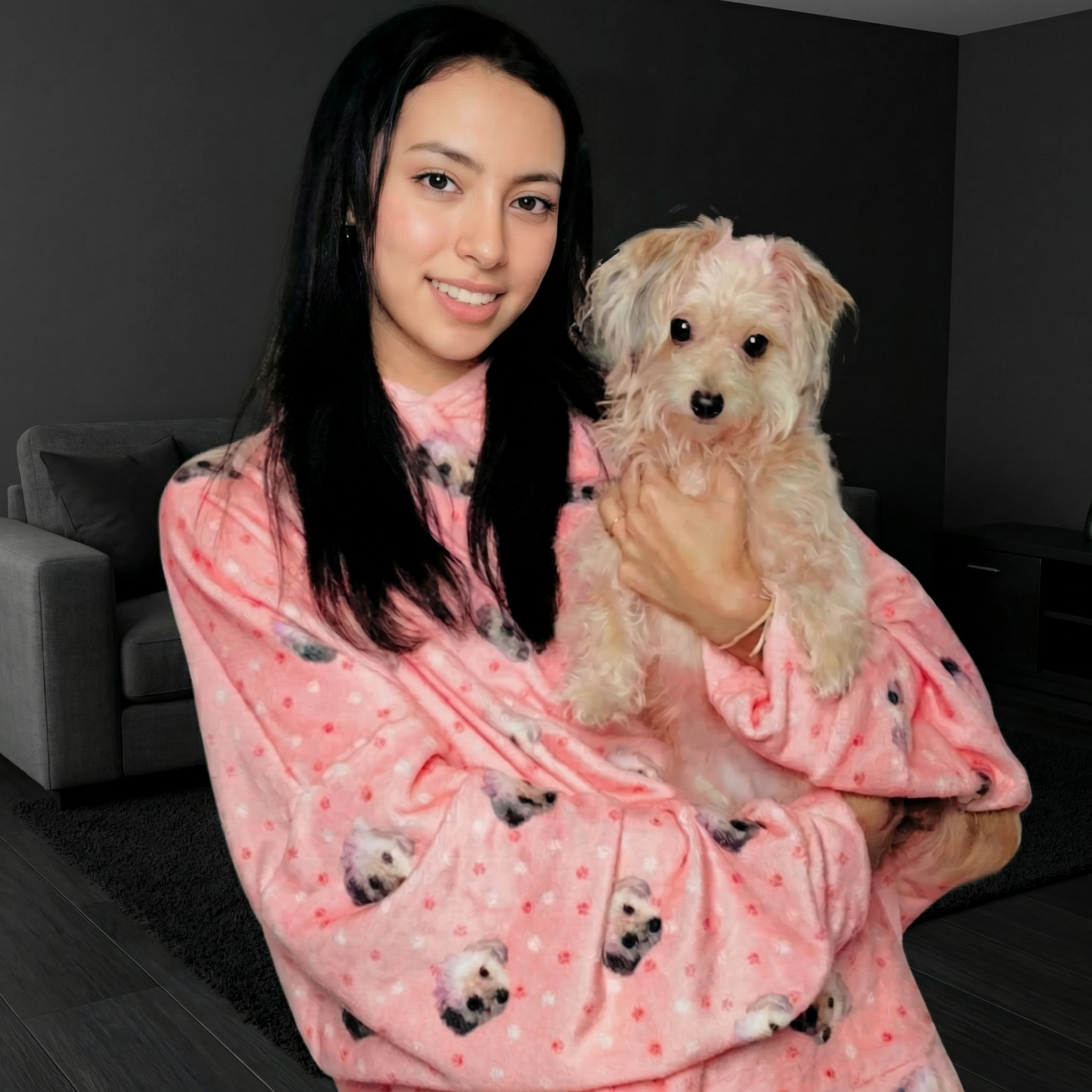Woman in pink dog-print blanket holds fluffy dog in cozy modern living room.