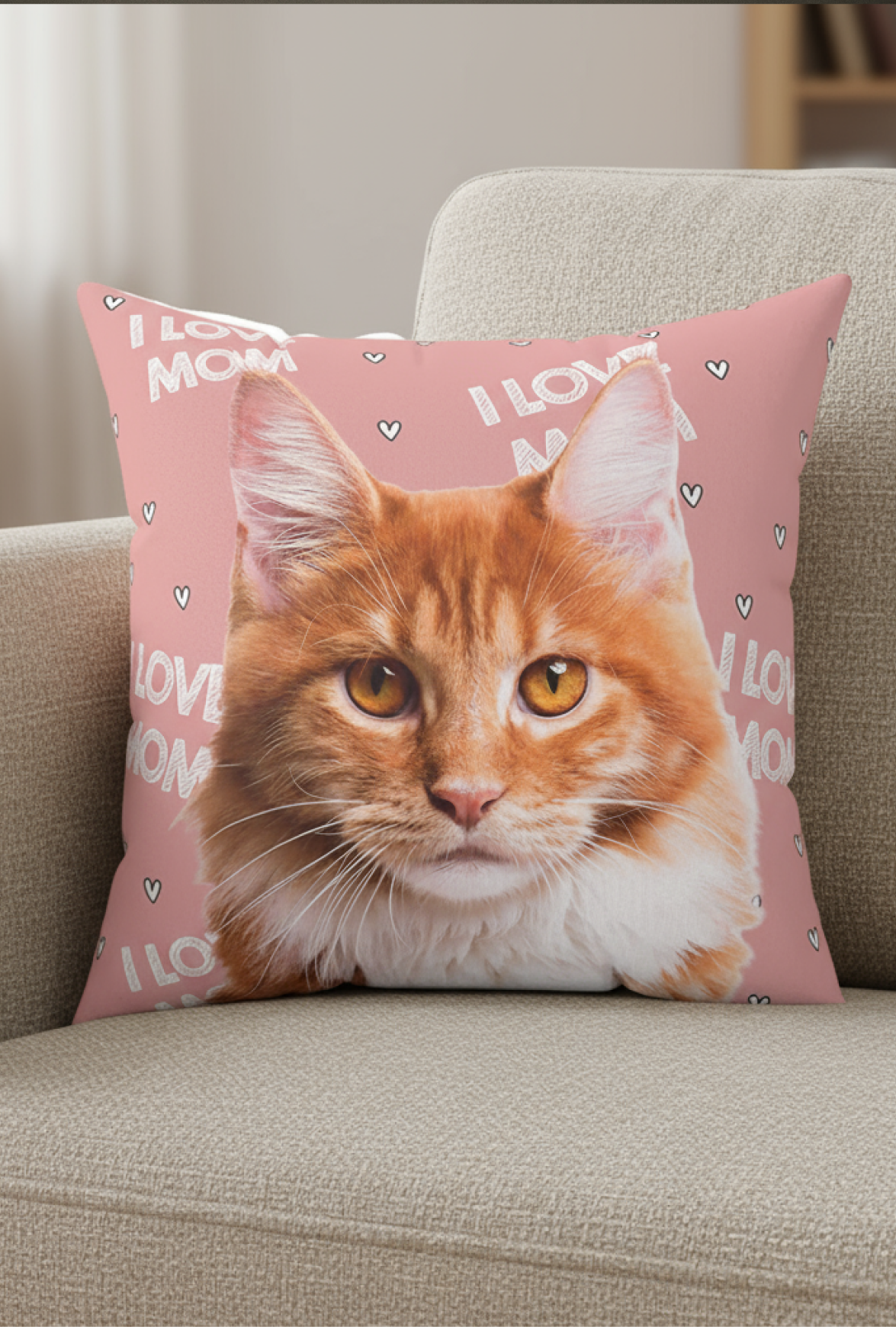 A square throw pillow featuring a large portrait of an orange and white fluffy cat (likely a Maine Coon) rests on a beige upholstered chair or couch. 