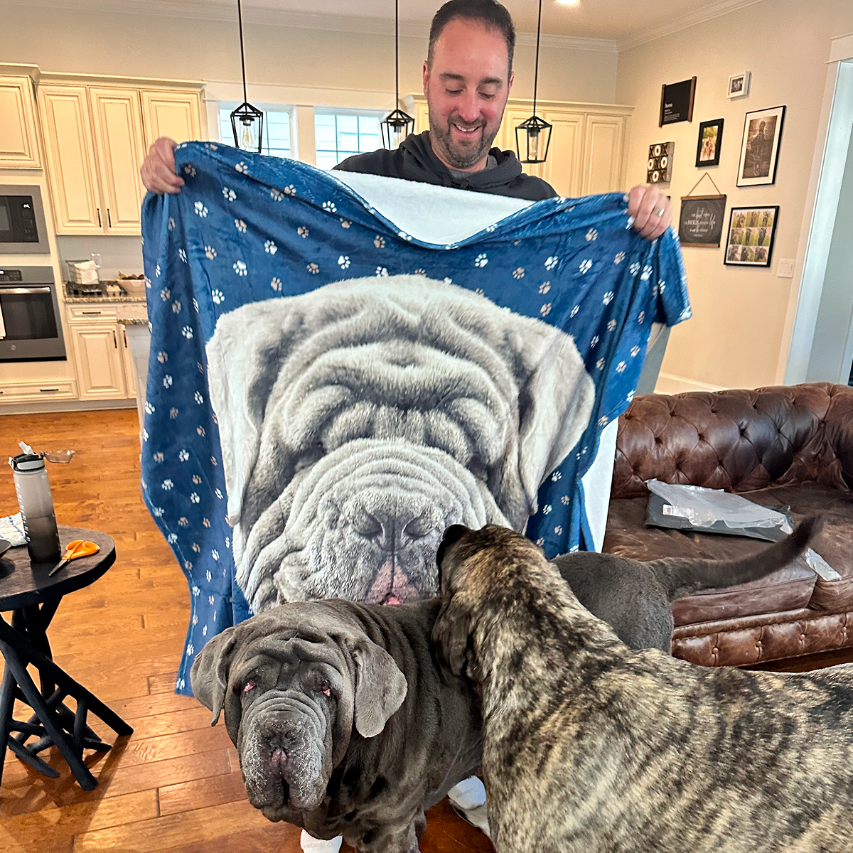 A man holds a holding up a blanket decorated with a realistic portrait of his dog.