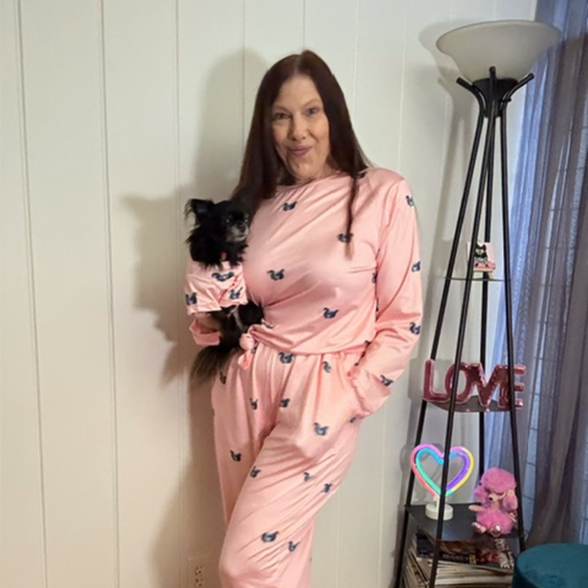 Woman holding a dog, both wearing matching pink outfits with small designs.