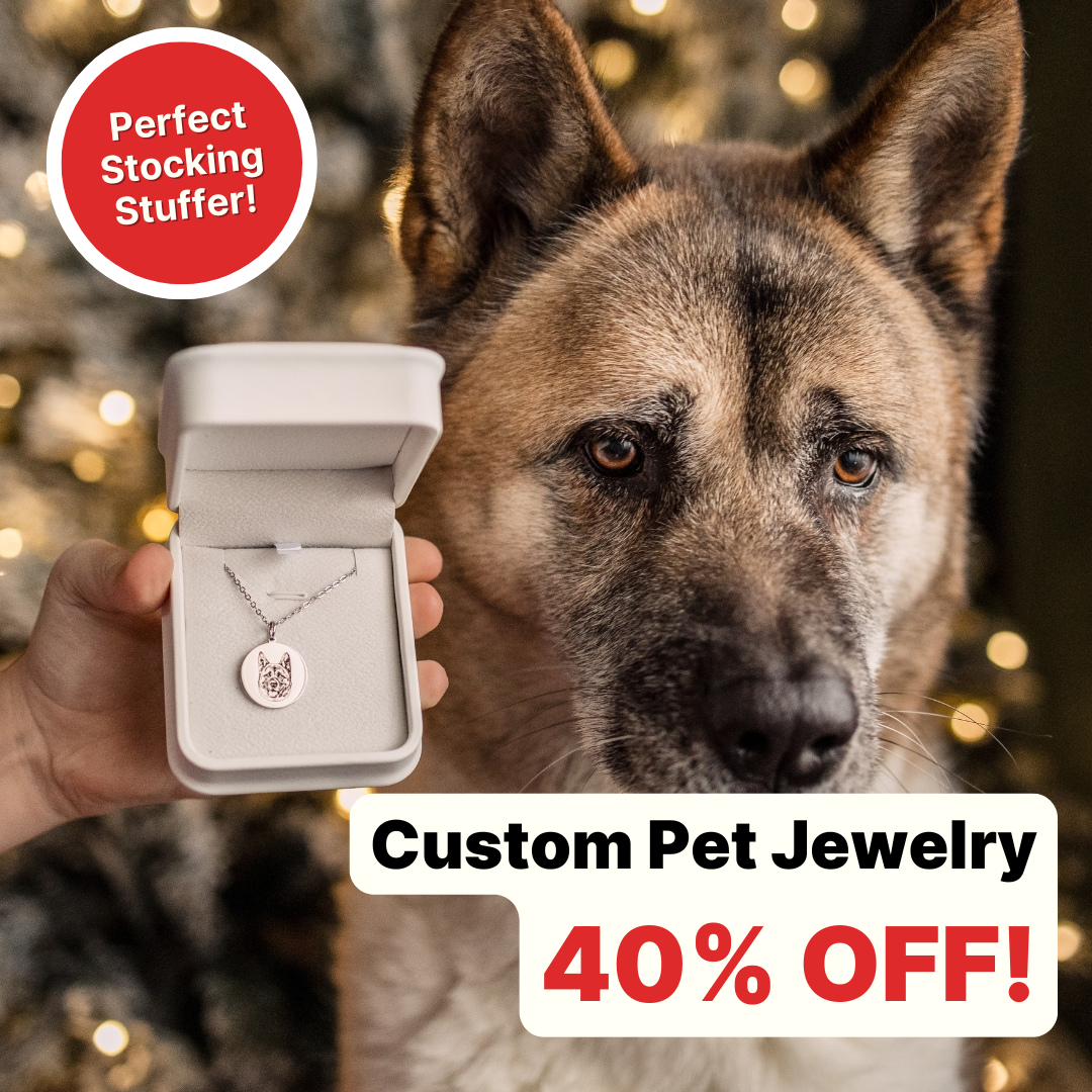 A close-up image of a large, brown and black dog (likely a German Shepherd or Akita) looking directly at the camera, with a blurred background of festive lights. A hand holds open a white jewelry box in the foreground, displaying a silver necklace with a custom pendant shaped like the dog's head.