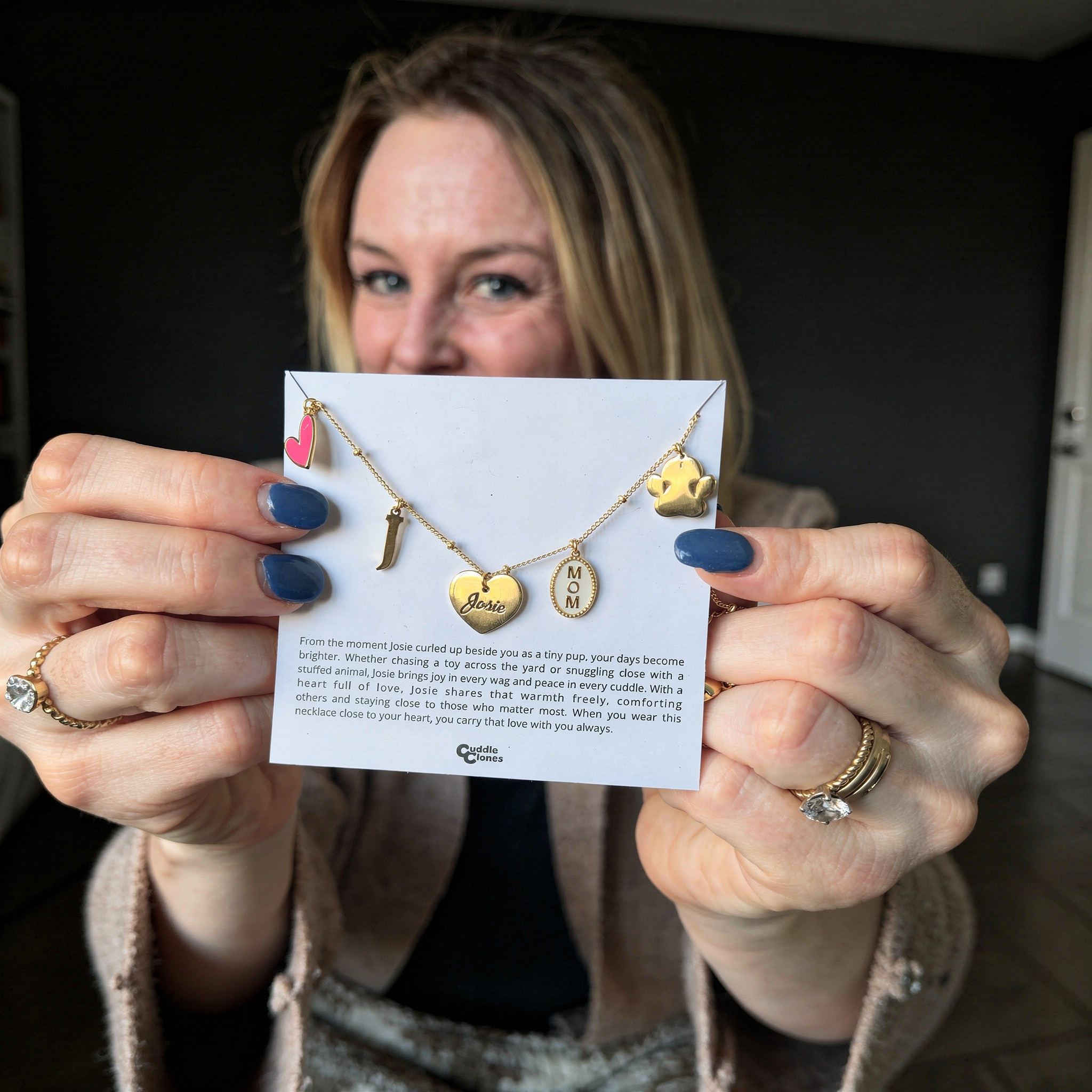 Woman holding Cuddle Clones charm necklace card with heart, letter J, Josie, MOM, and paw